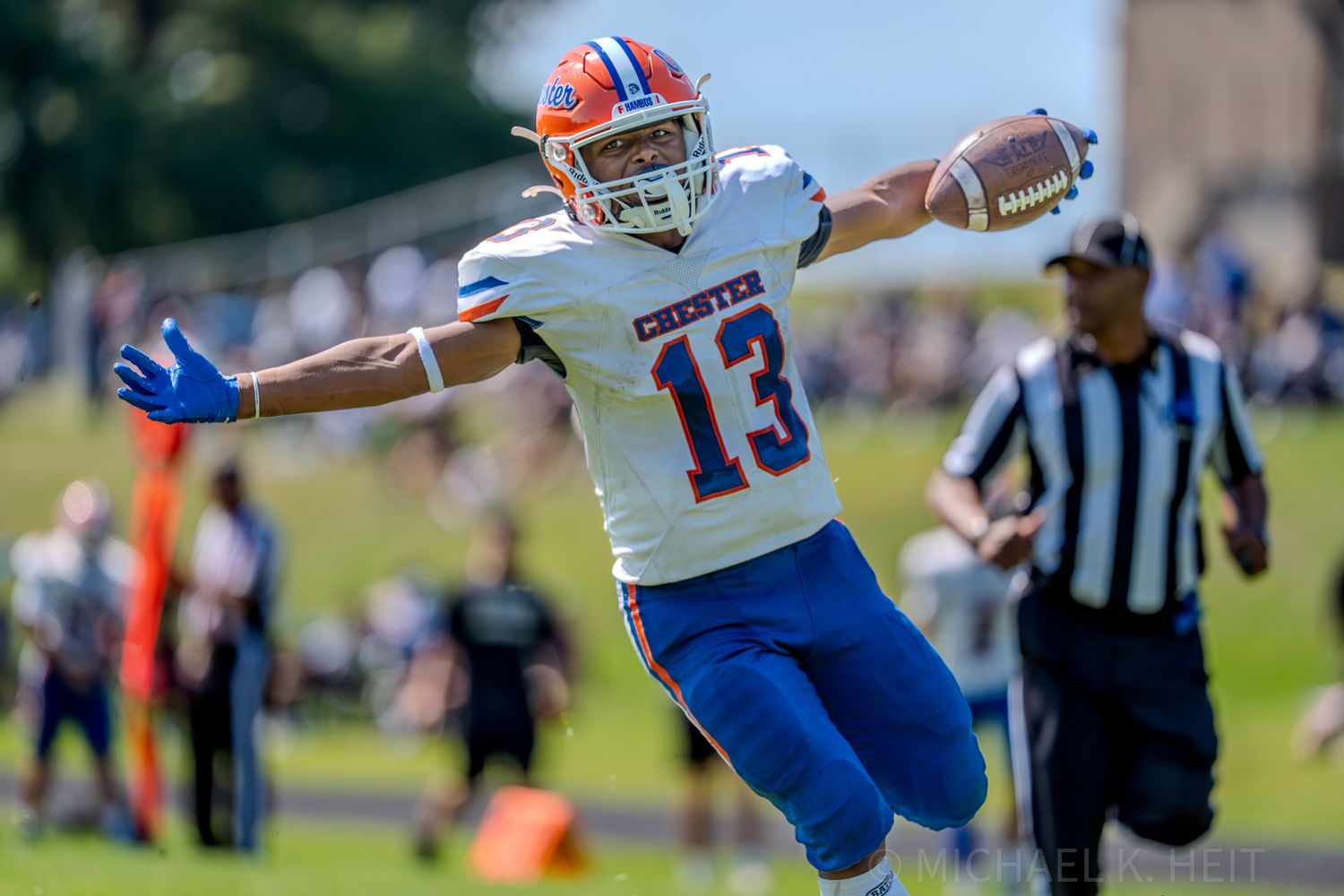 Football players in blue and white uniforms reach for the ball during an offensive play.
