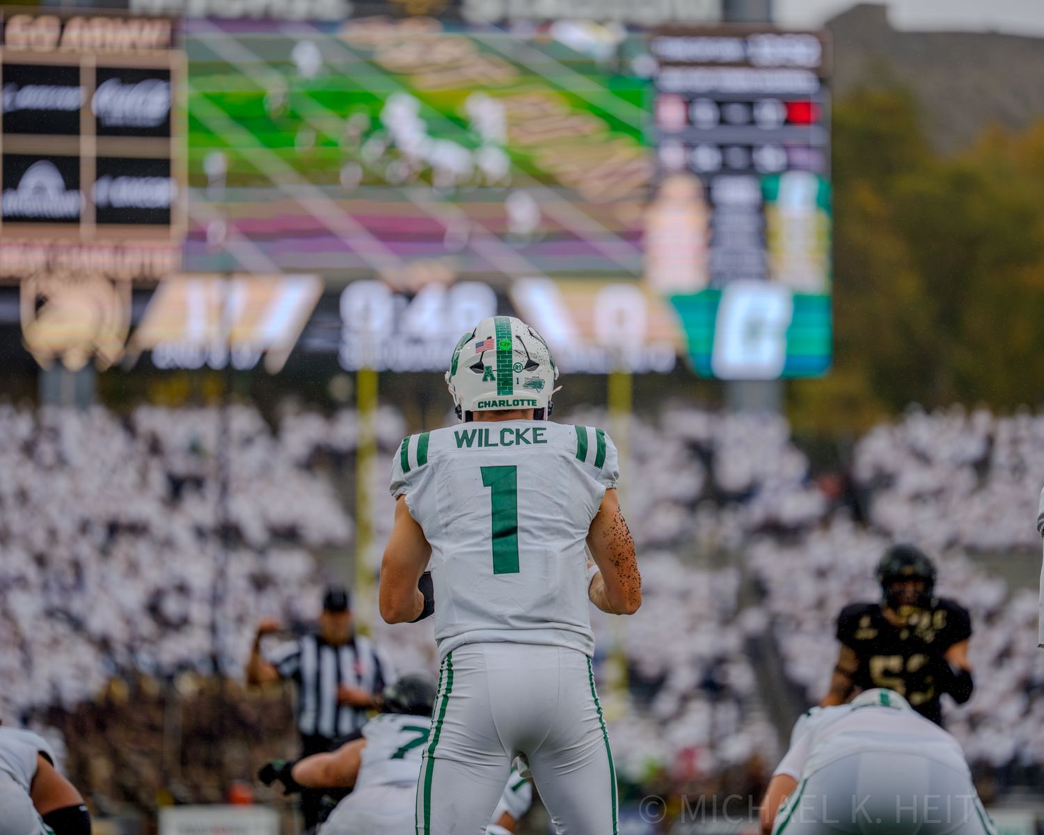 Football players in white uniforms line up on the field during a game.