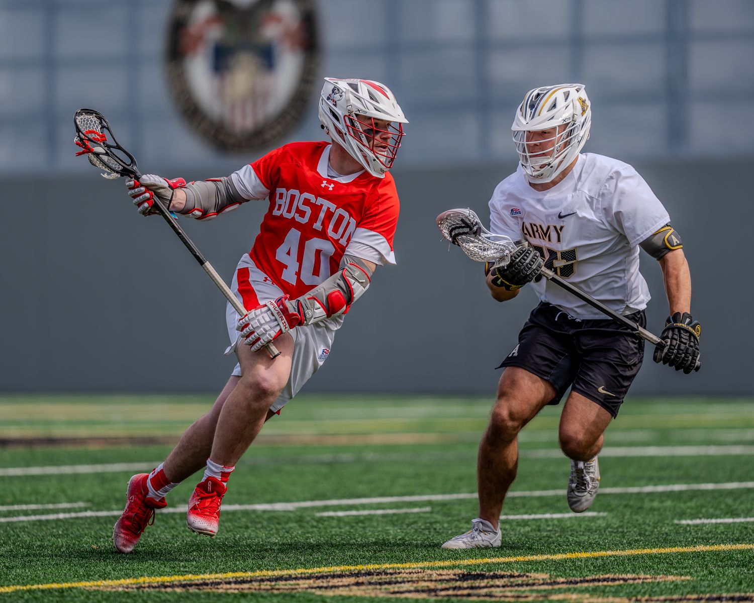 Lacrosse players in white and red uniforms battle for ball possession on the field.