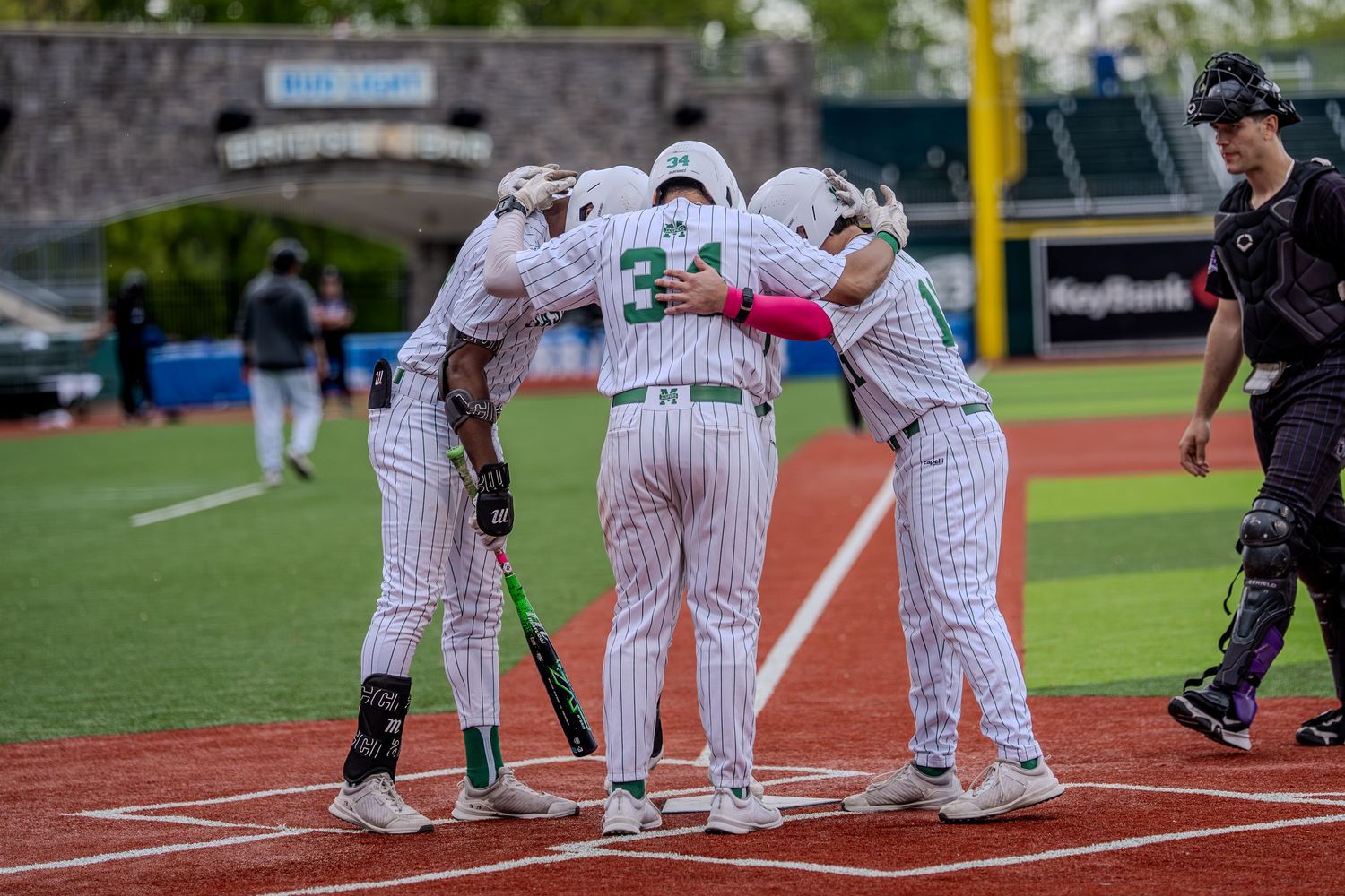 Baseball players in white pinstripe uniforms huddle together at home plate during a game.