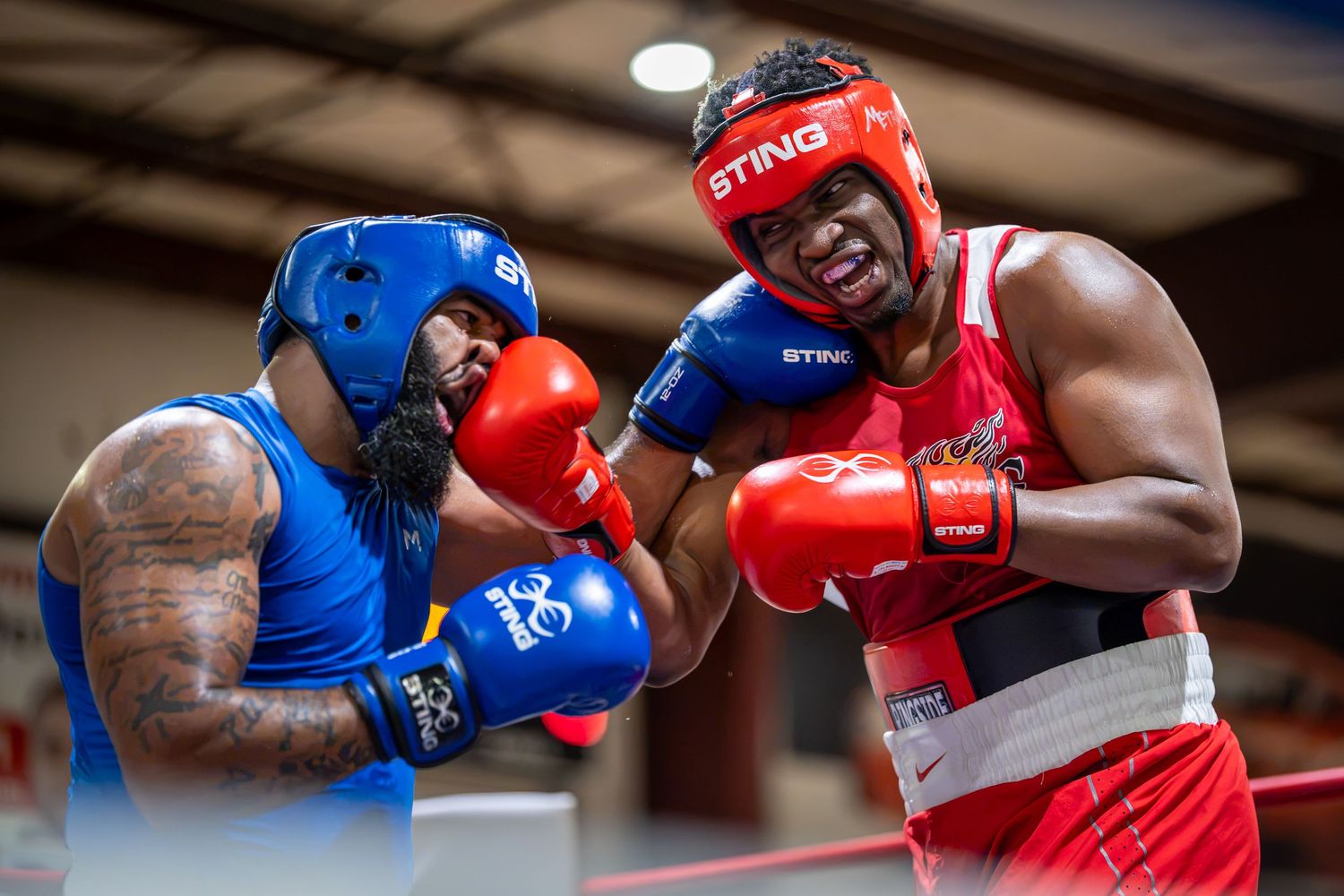 Two boxers sparring in a ring, one in blue gear and one in red gear, exchanging punches during an amateur boxing match.