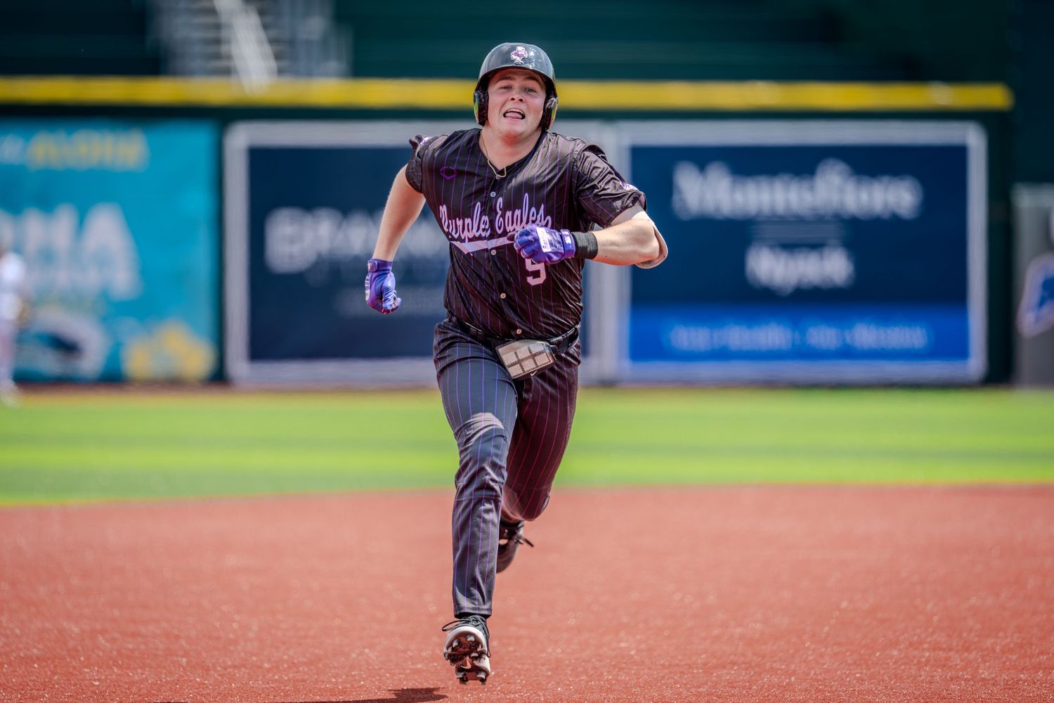 Baseball player in purple uniform sprinting bases during a game in a professional stadium.