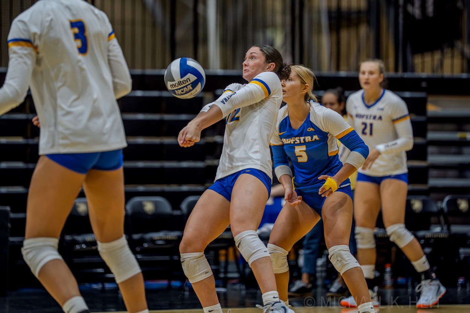 Volleyball players prepare to receive serve during competitive indoor match.