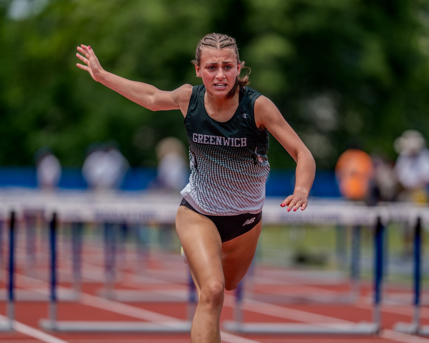 Track athlete in black and gray uniform leaping over hurdle during outdoor competition.