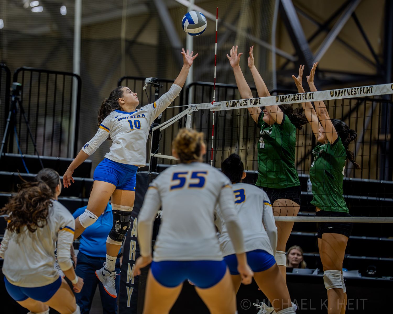 Volleyball players from opposing teams battle at the net during a competitive indoor match.