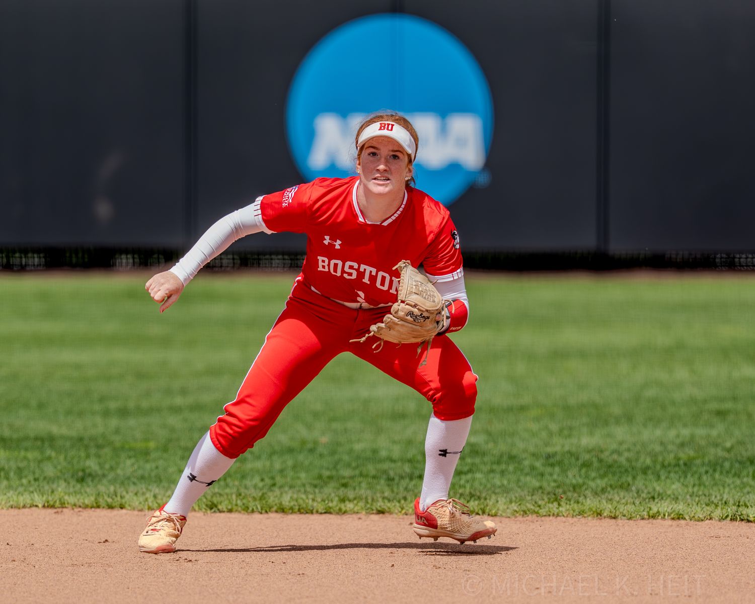 Infielder in red Boston uniform ready in defensive stance during NCAA game.