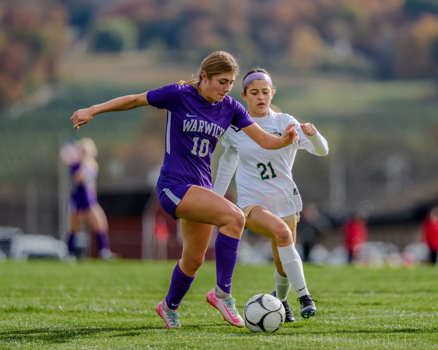 Soccer players battle for possession of the ball during an intense match between teams in purple and white uniforms.