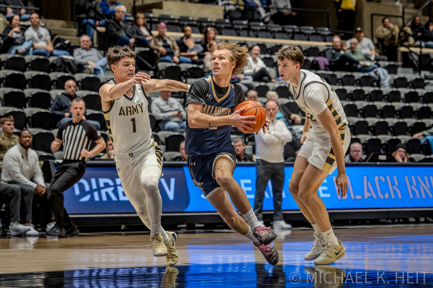 Basketball player drives between two defenders during an intense college basketball game.