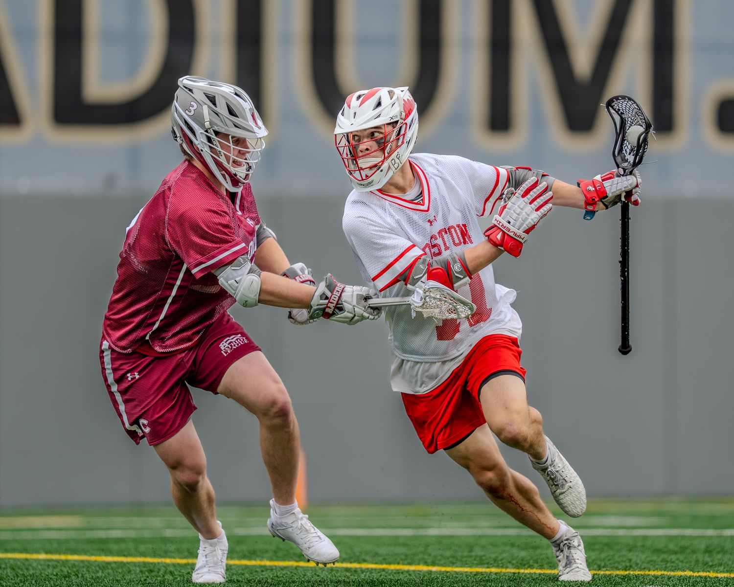 Lacrosse players in red and white uniforms battle for possession during an intense game.