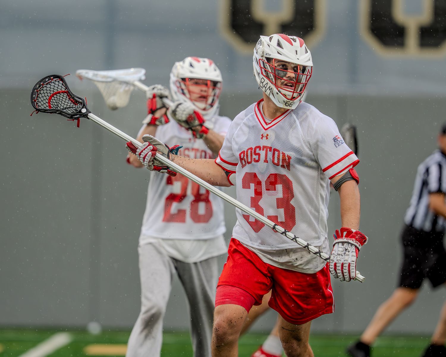 Lacrosse players from opposing teams position themselves during an intense game moment.