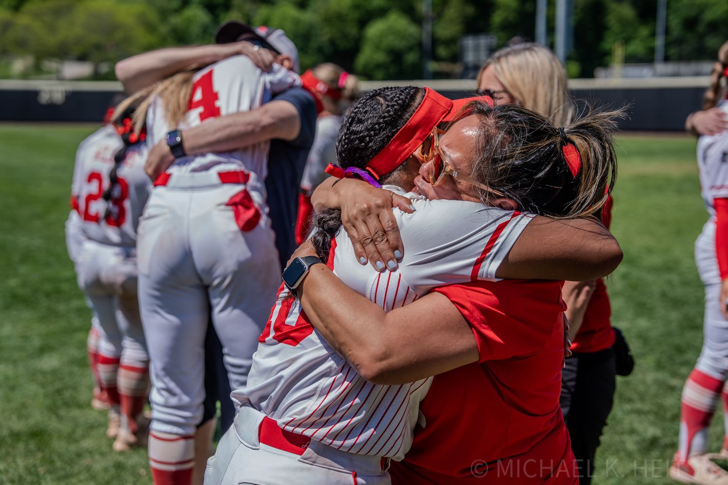 Athletes in white baseball uniforms embrace supporters during an emotional field celebration.