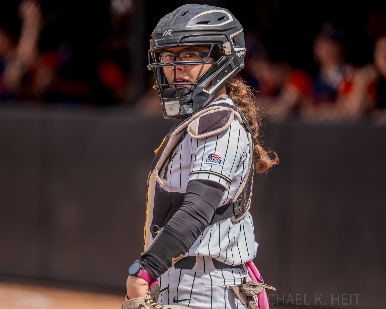 Softball catcher in pinstriped uniform and protective gear looking over shoulder.