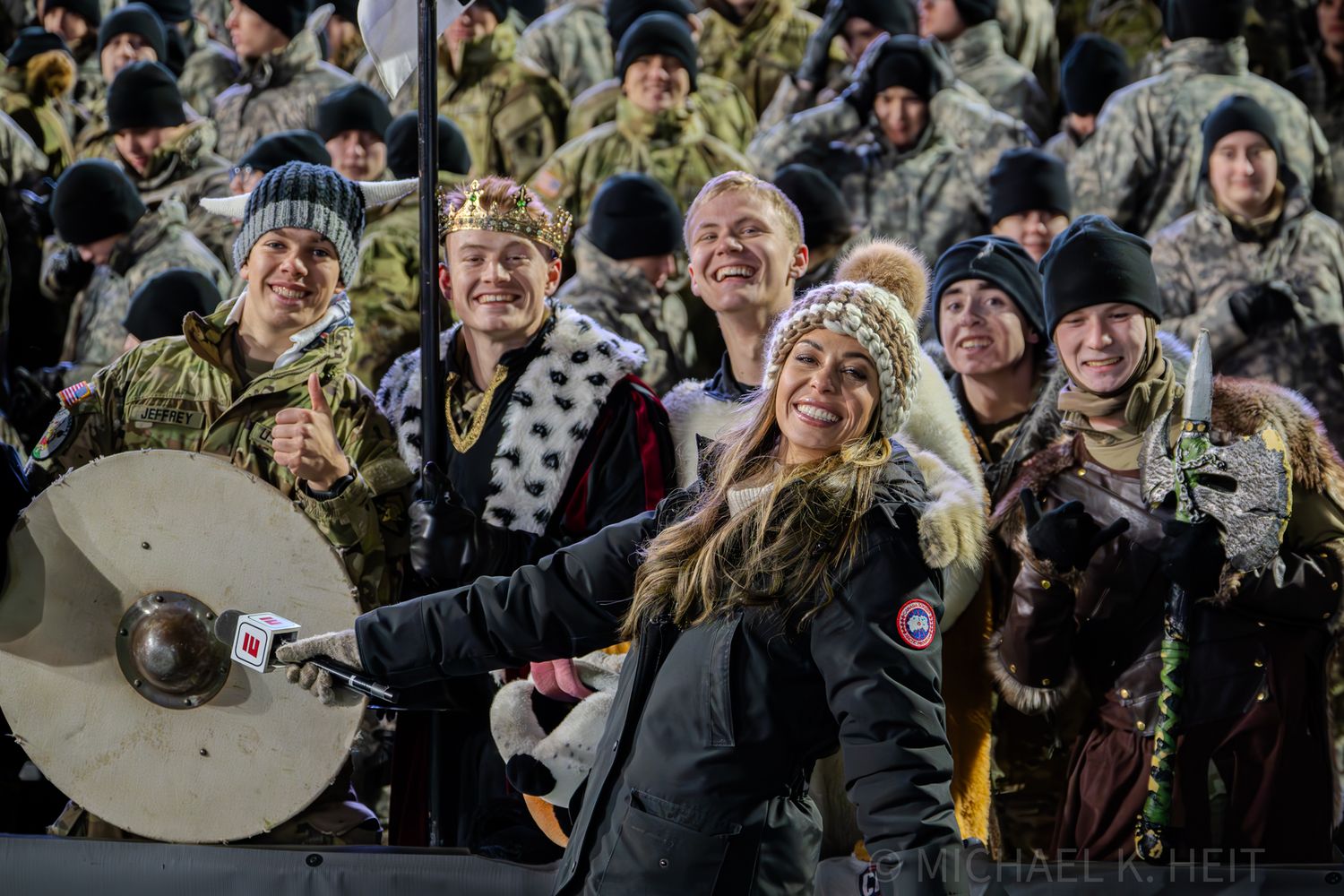 Enthusiastic fans in winter gear cheer from the stands during a football game.