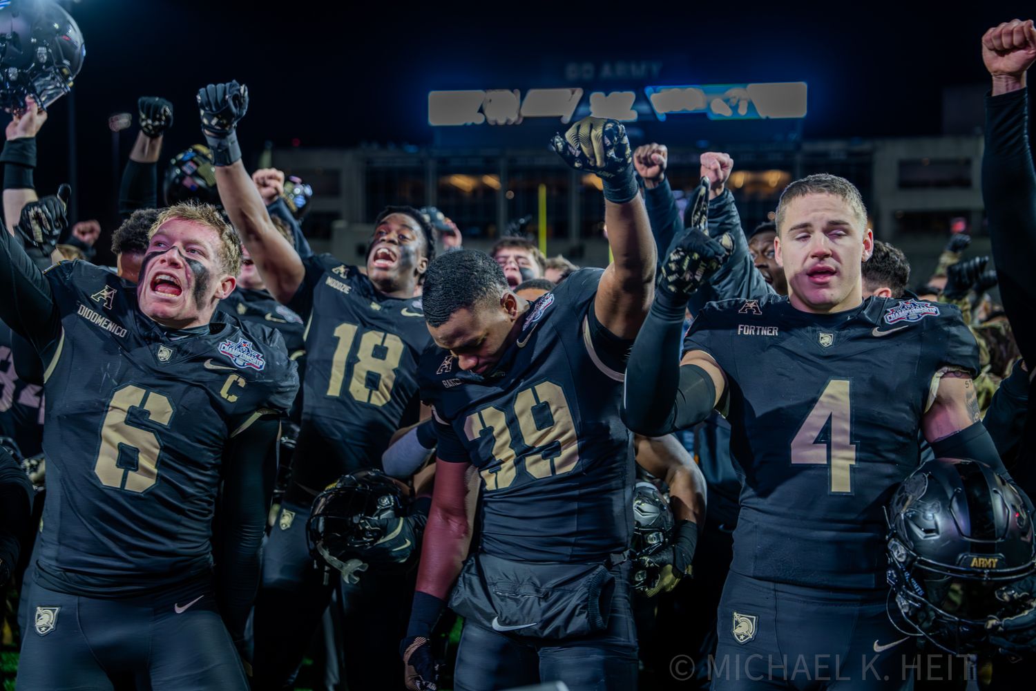 Football team celebrates in dark uniforms after scoring during a night game.