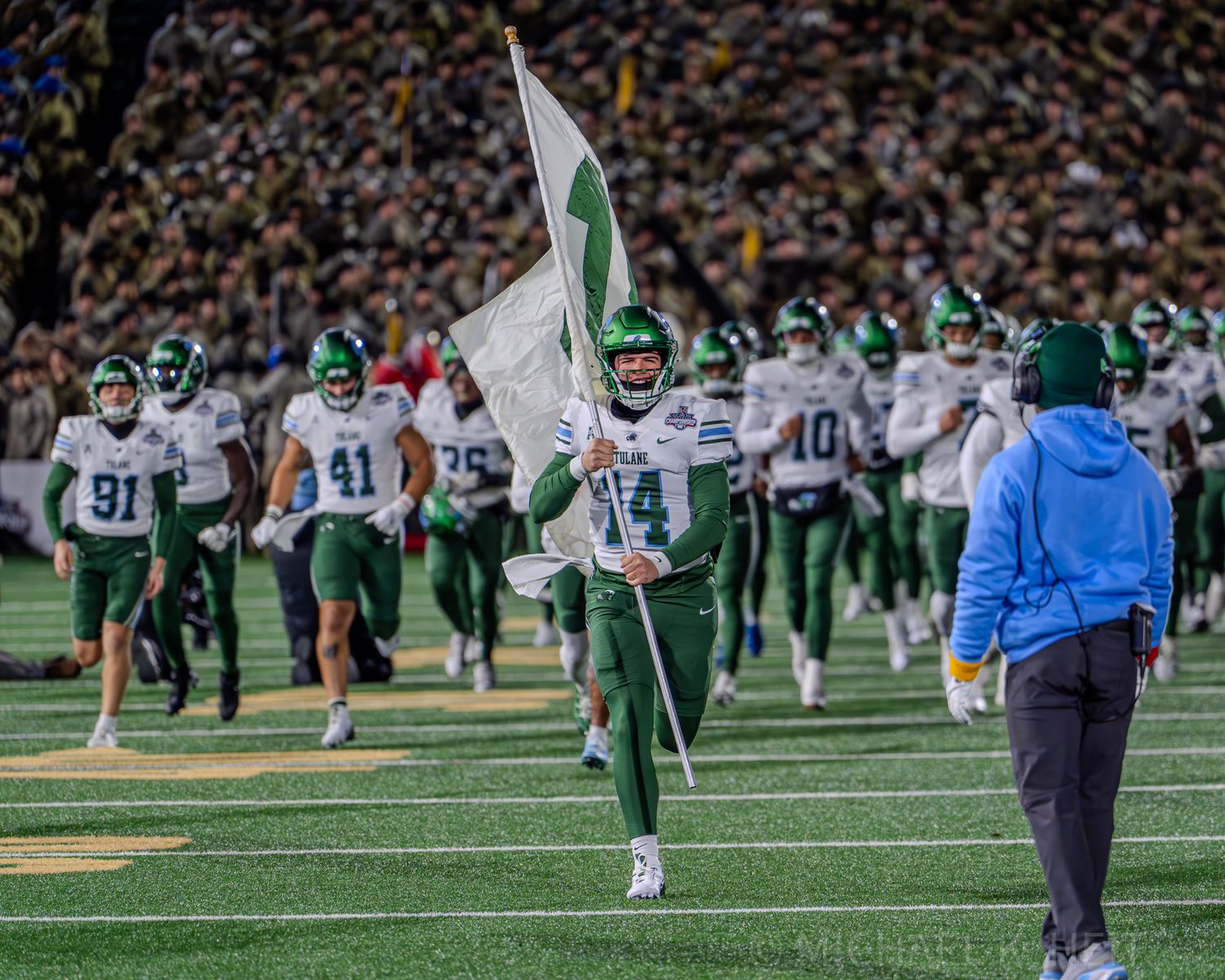 Football players in white and green uniforms spread across the field during game action.