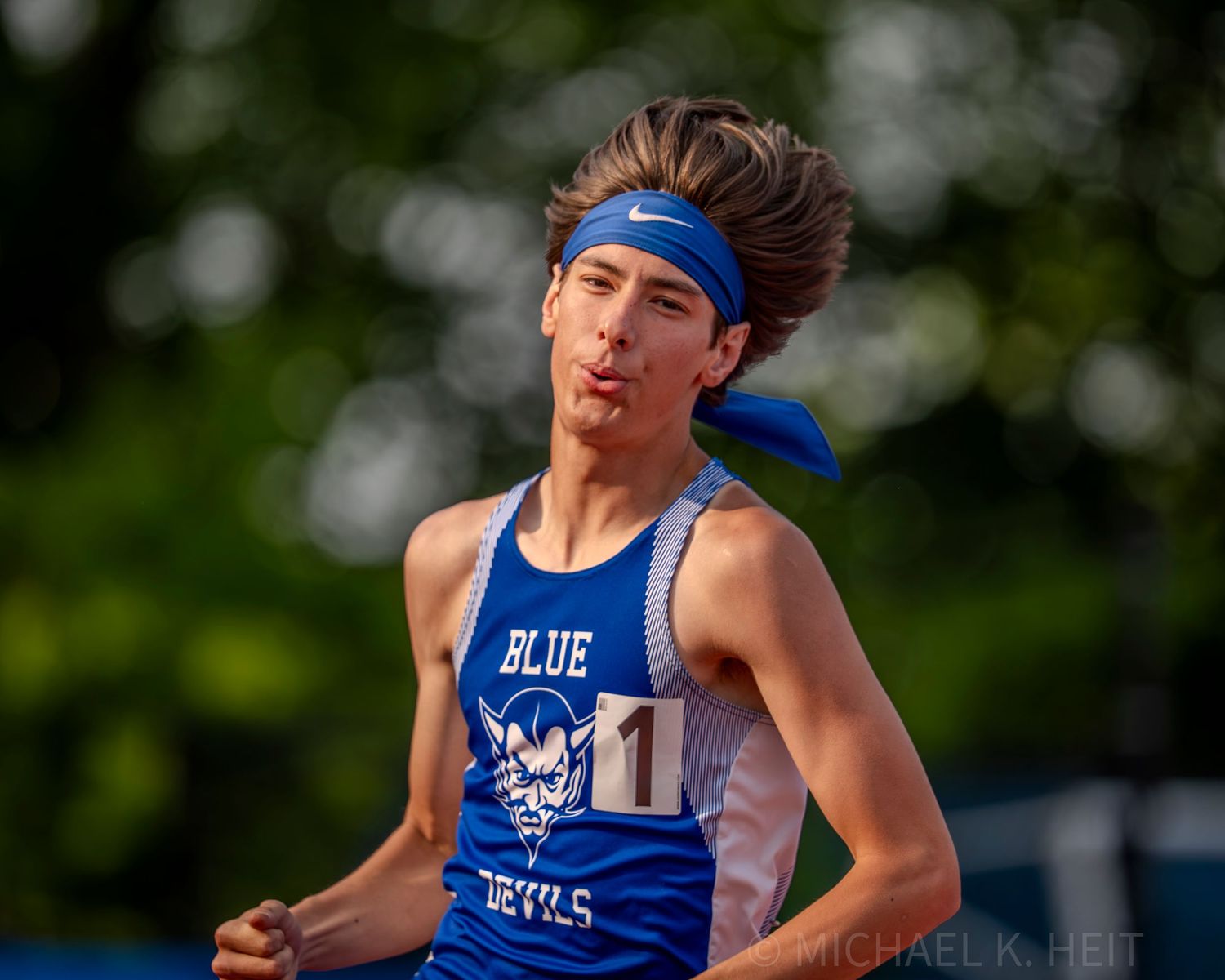 Track athlete in blue uniform competing at outdoor event.