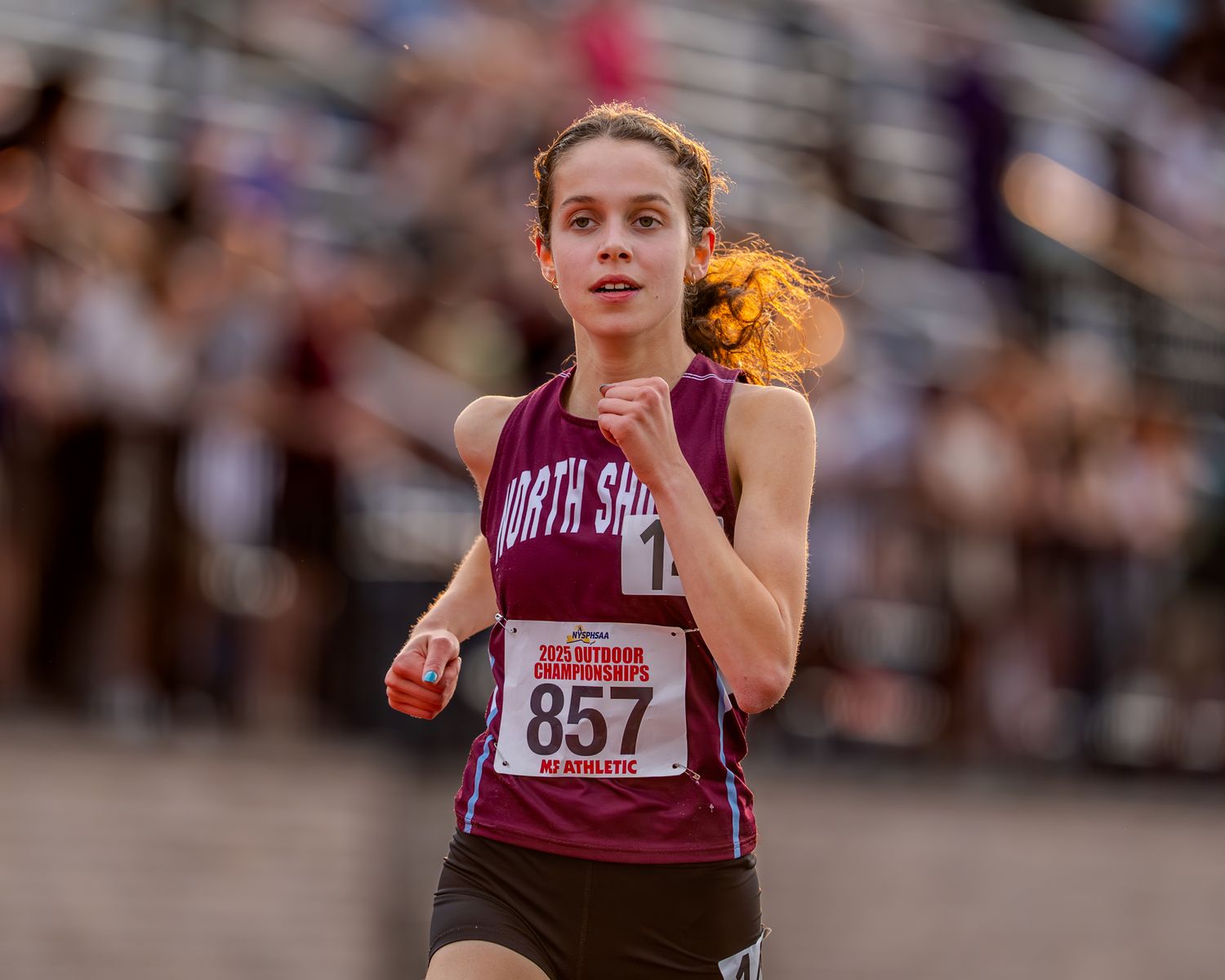 Athletes compete in track and field events at a high school competition with a large crowd in attendance.