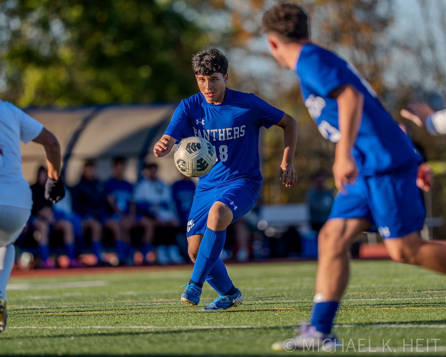 Soccer player in blue uniform performs a sliding tackle during an outdoor match on grass field.