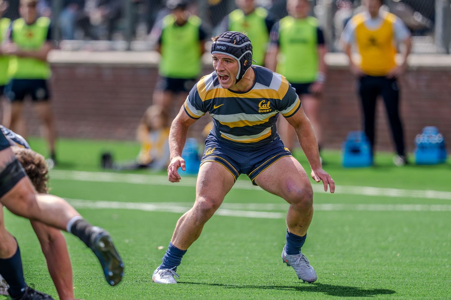 Rugby players compete for possession during an intense match on an artificial turf field.