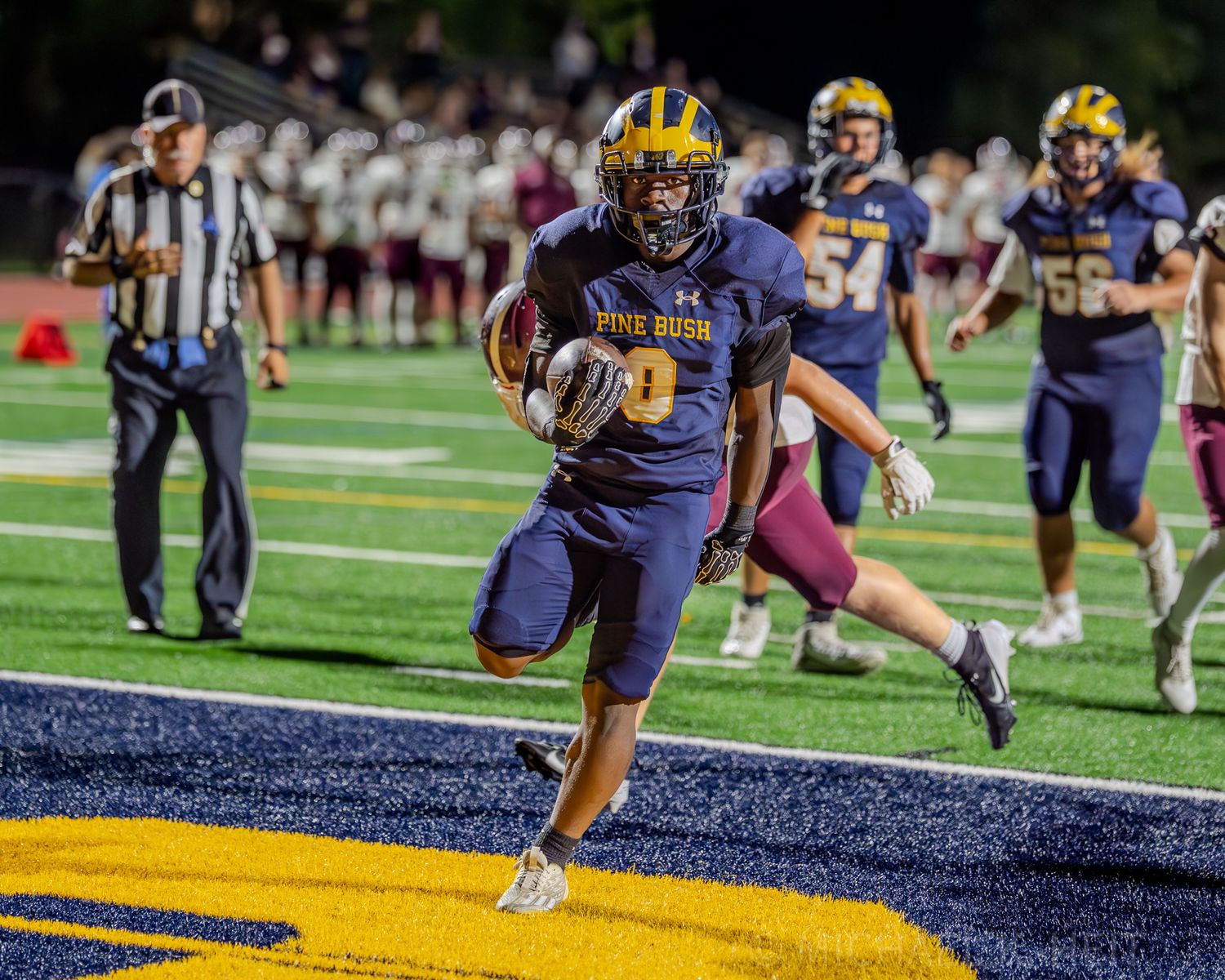 High school football teams face off on a sunny field with players in blue and yellow uniforms.