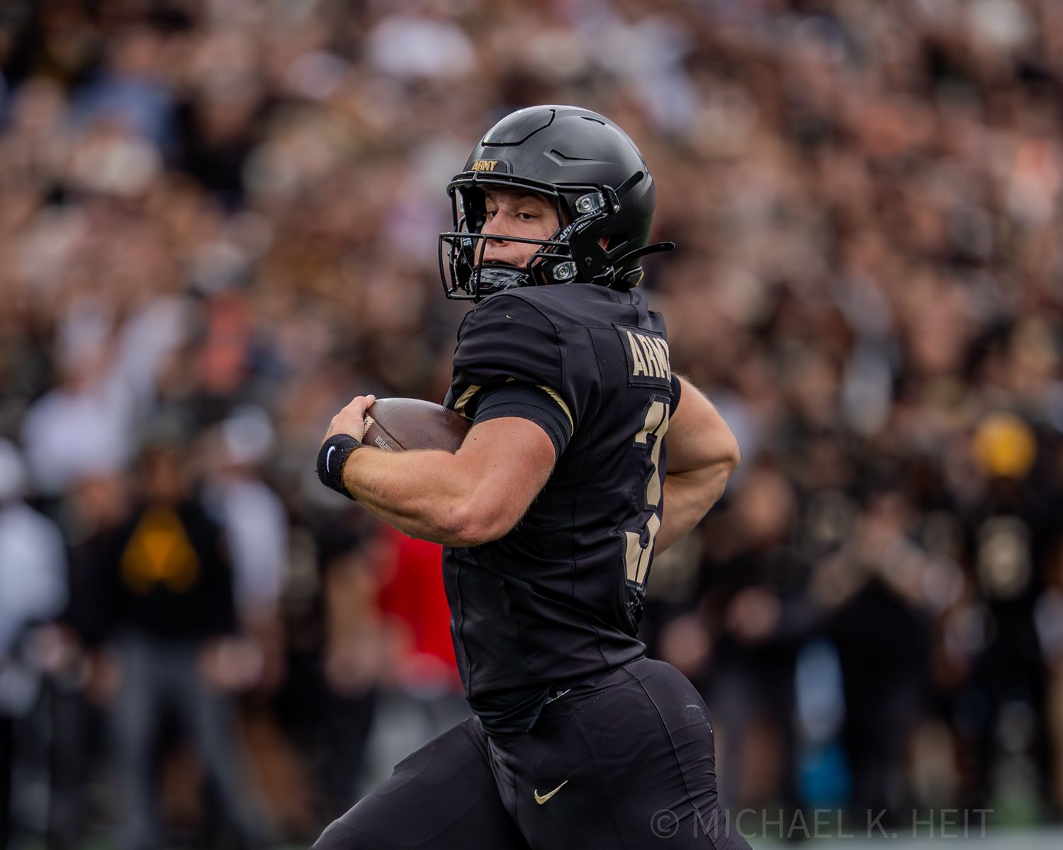 A player in black uniform runs with the football during a game.
