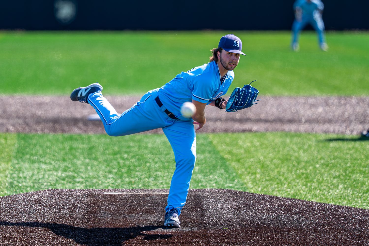 Baseball player in bright blue uniform pitches from mound during game.
