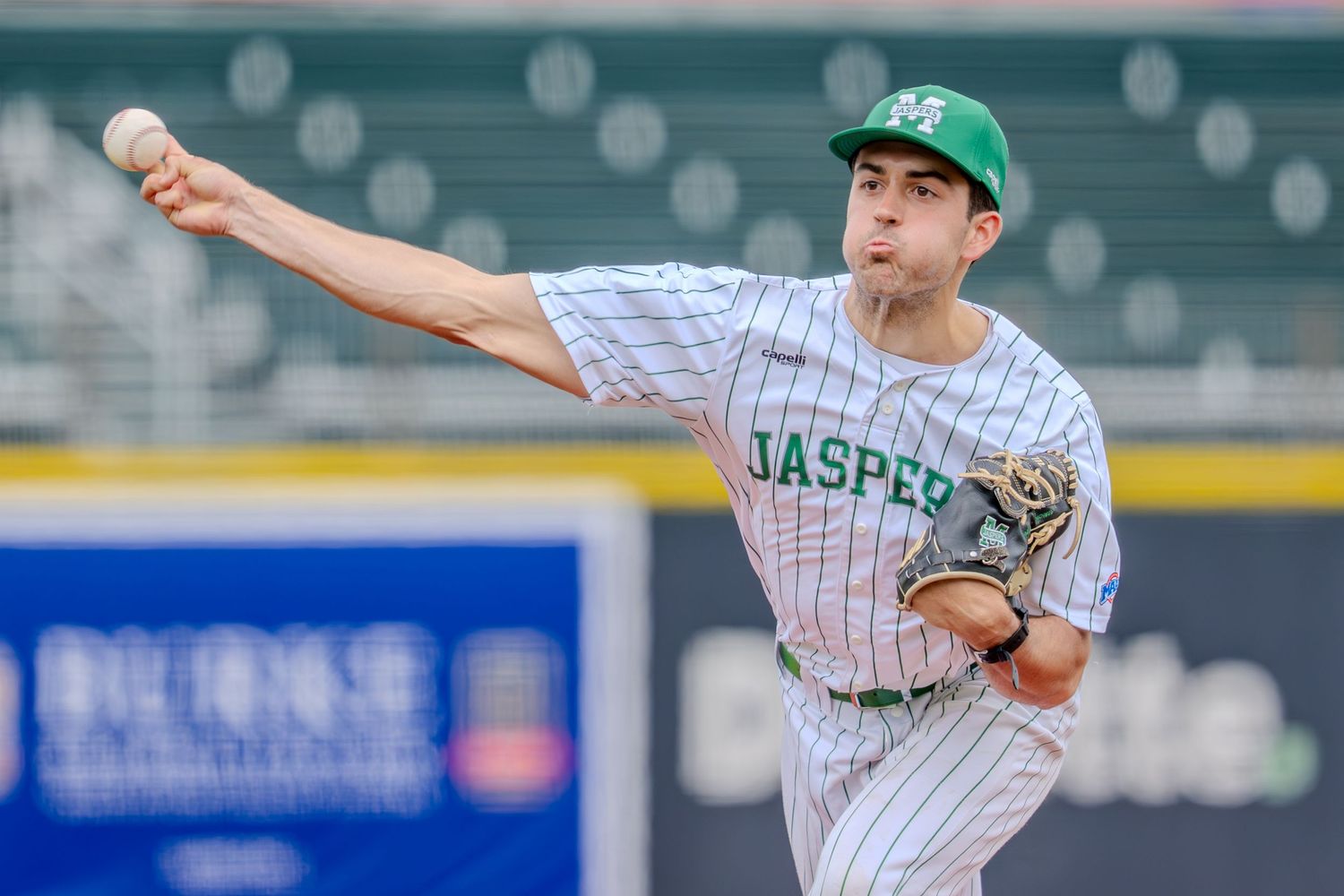 Jasper baseball pitcher in green and white pinstripe uniform delivering a pitch during a game.