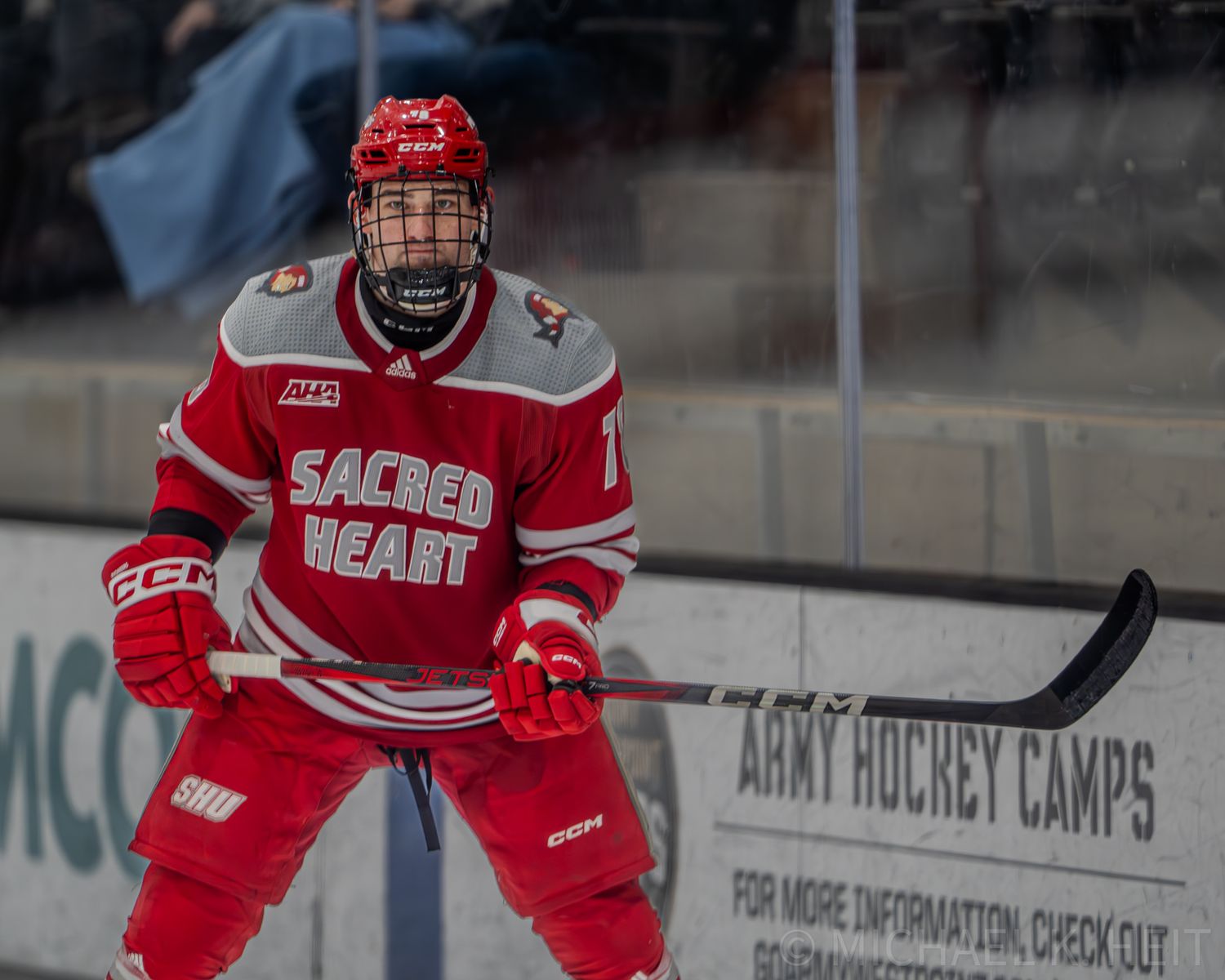 A hockey player in a Sacred Heart red jersey stands ready on the ice during a match.