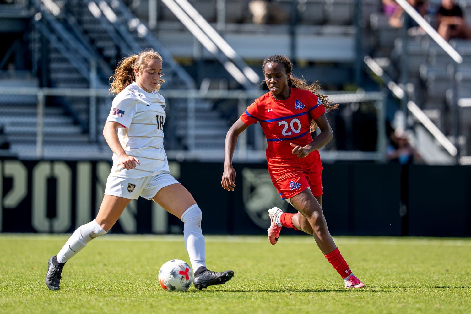Two female soccer players compete for the ball during a match, one in white and one in red uniform.