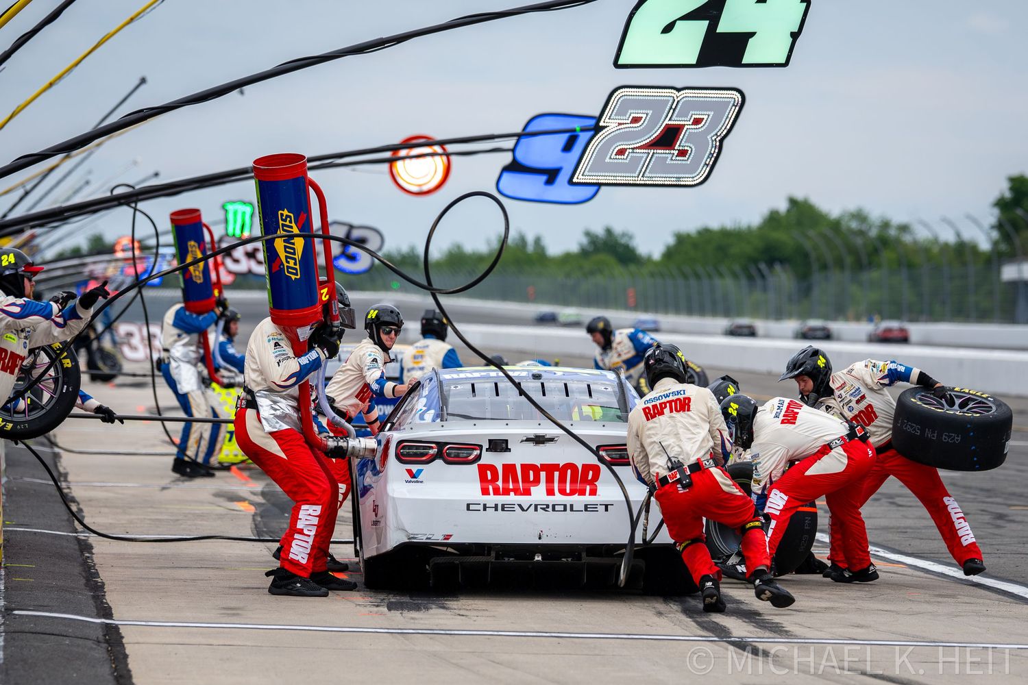 NASCAR pit crew services the Raptor Chevrolet race car during a pit stop at a busy racing event.