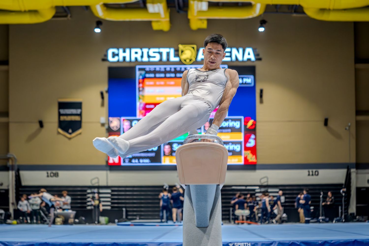 Male gymnast performs pommel horse routine at Christl Arena competition, showcasing strength and balance.