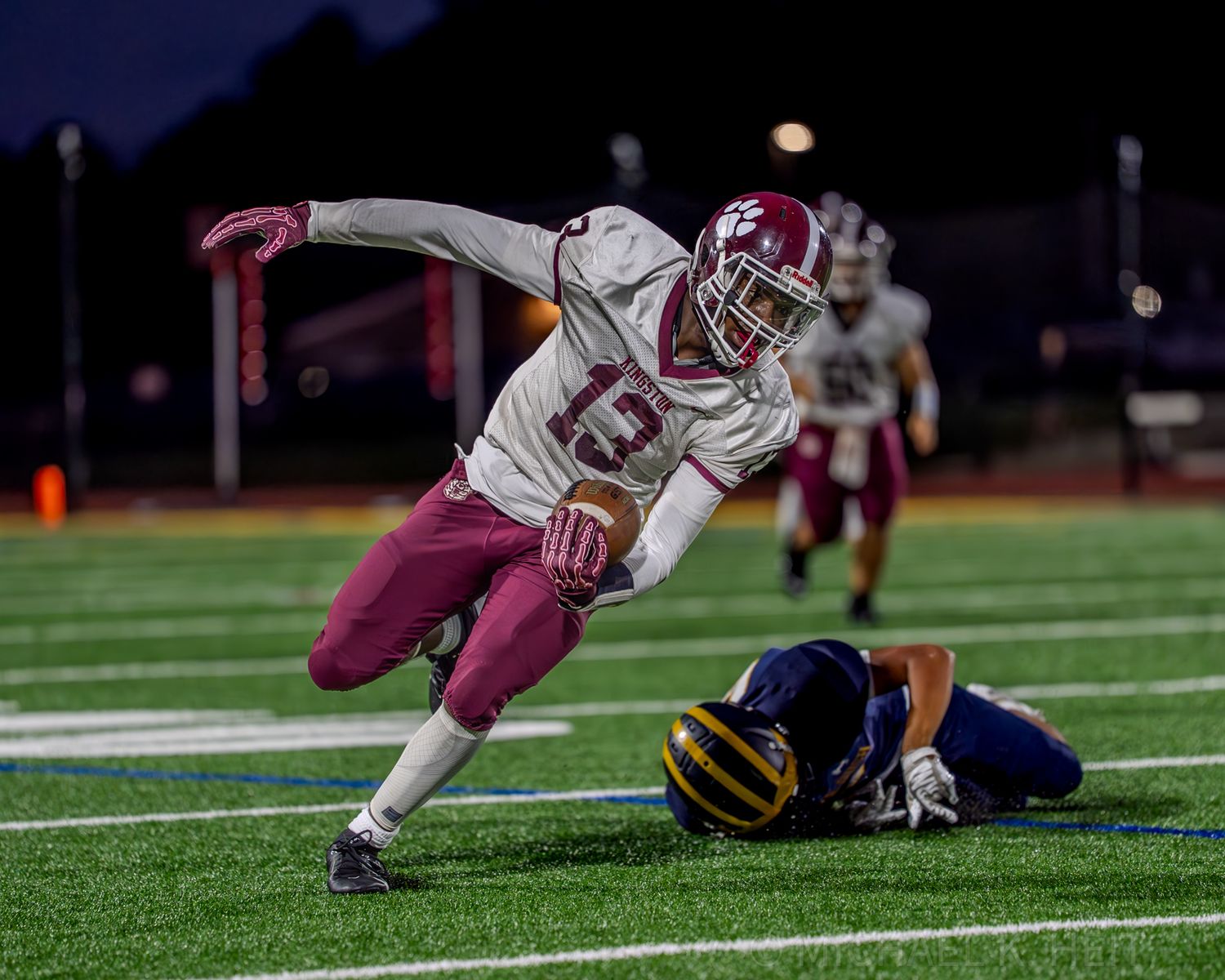Football players tackle opponent during nighttime game on turf field.