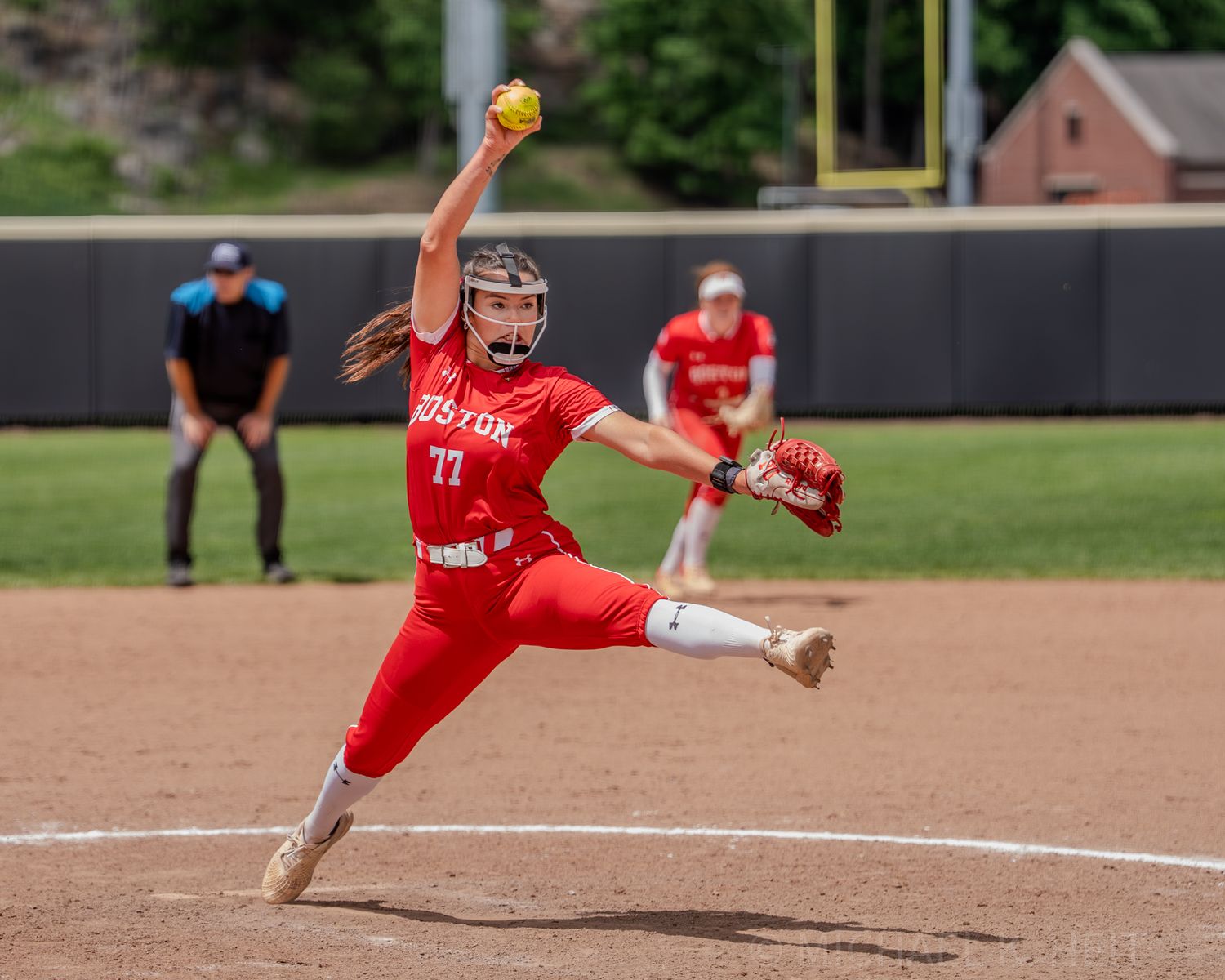Softball pitcher in red uniform mid-delivery during intense game action.
