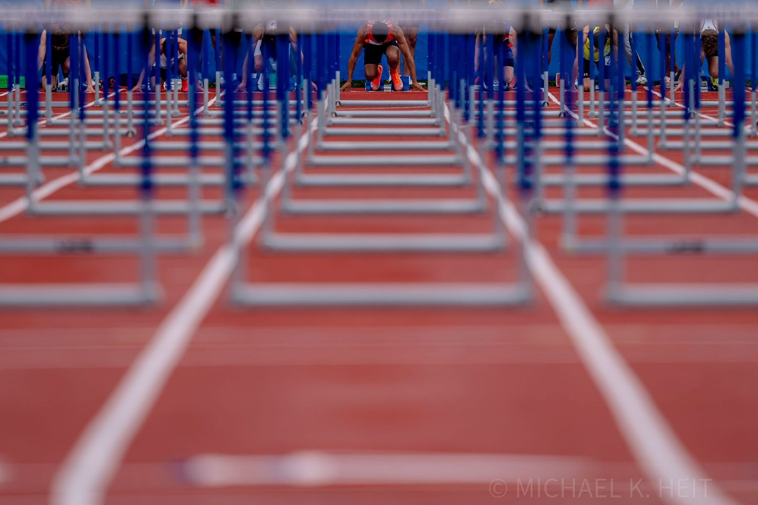Row of blue hurdles lines up on a red track awaiting competitors.