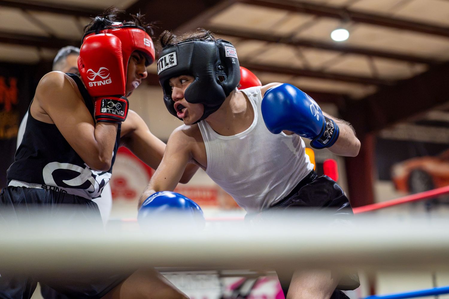 Two young boxers sparring in a boxing ring, wearing headgear and gloves during a competitive match.
