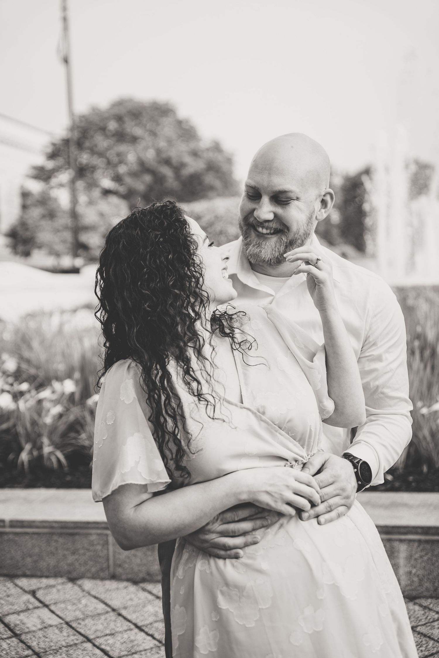 Black and white romantic portrait of couple embracing near a fountain in an outdoor setting.