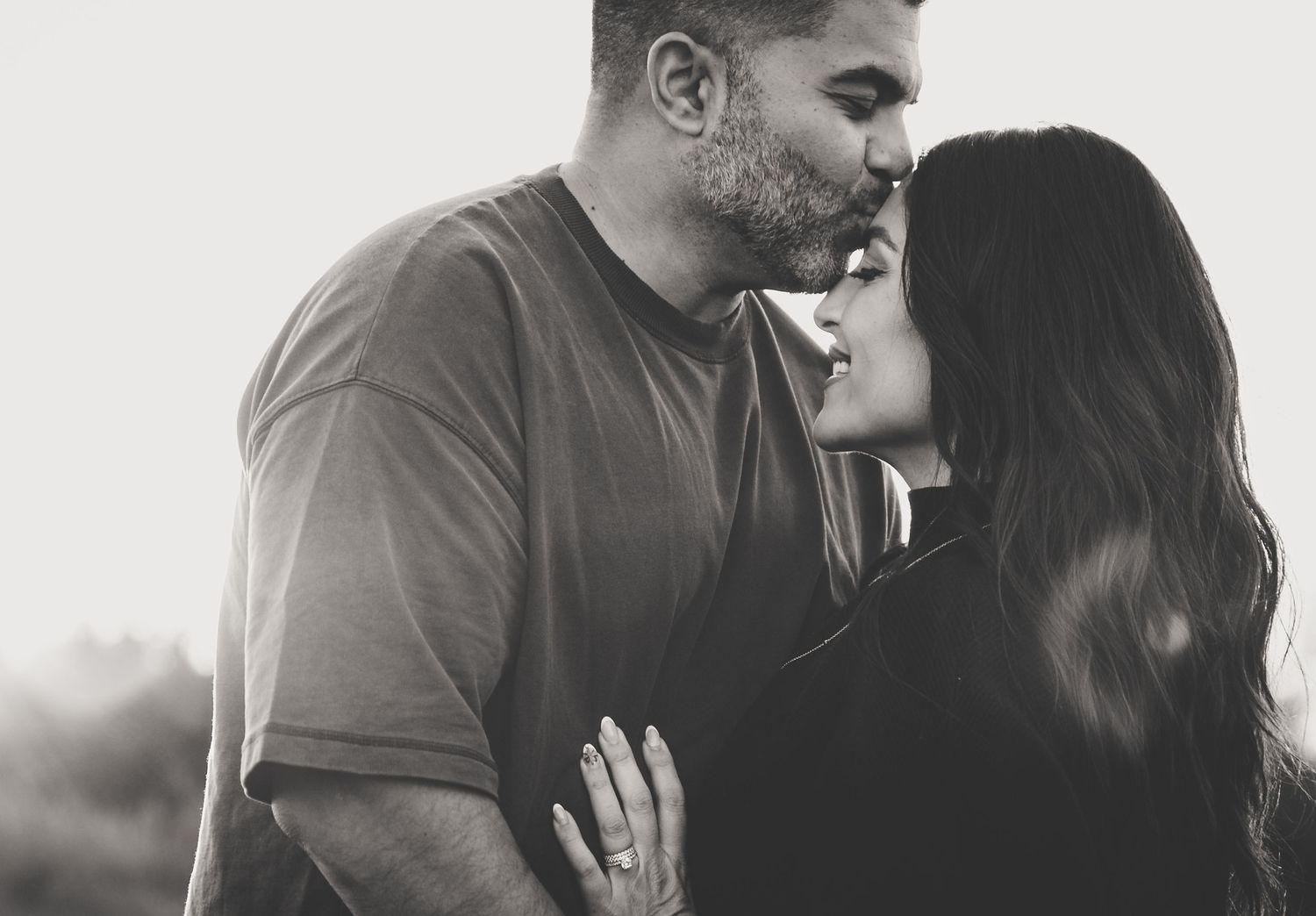 A romantic black and white close-up of a couple sharing a tender kiss outdoors at golden hour.