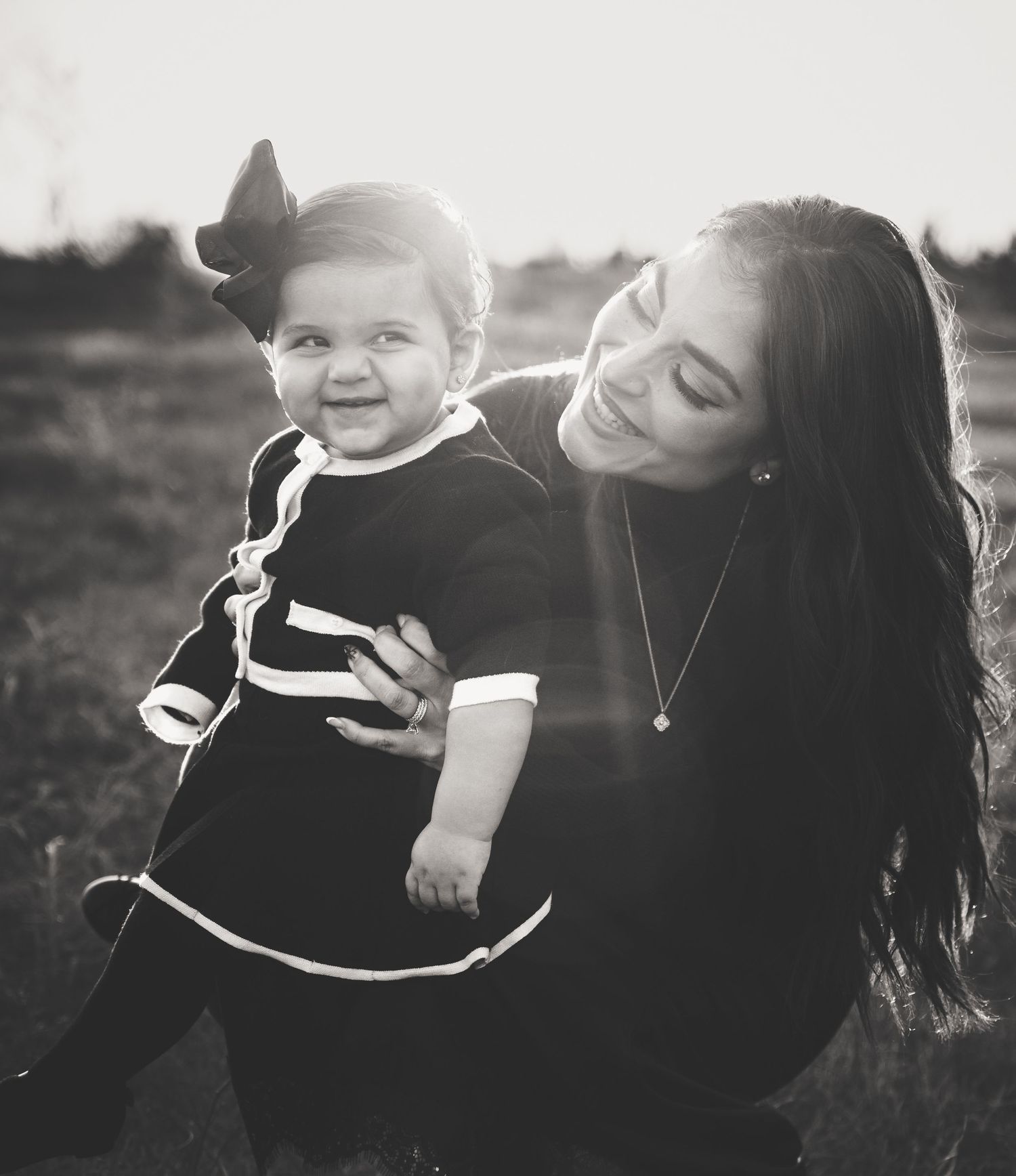 A black and white photo of a smiling mother holding her happy baby girl outdoors.