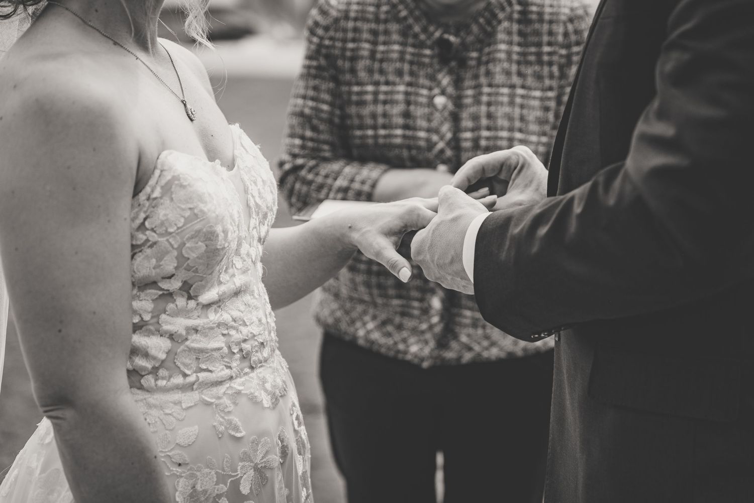 Black and white close-up of groom placing wedding ring on brides hand during ceremony.
