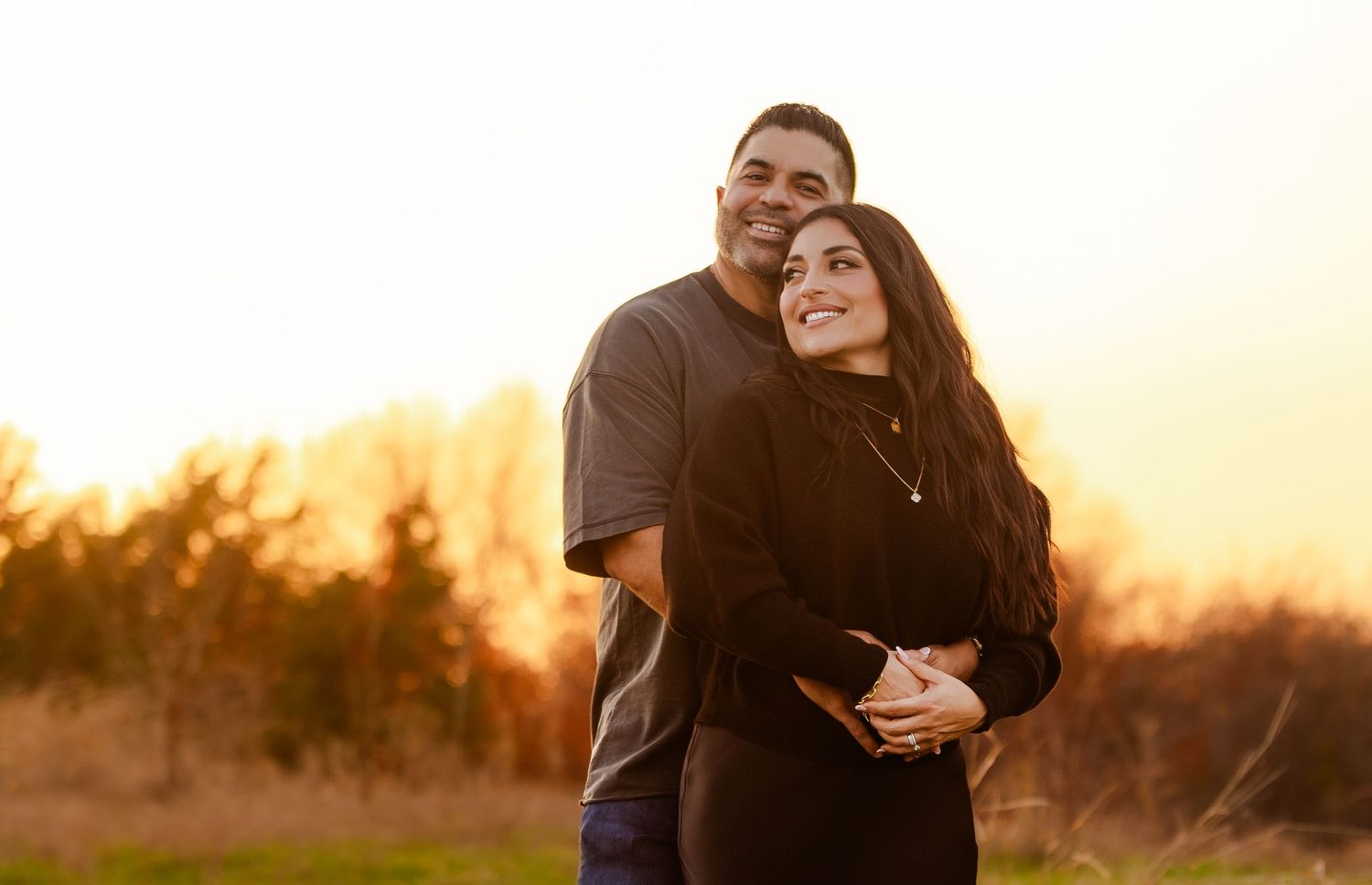 A couple embraces warmly while gazing upward together during a beautiful golden sunset outdoor portrait.