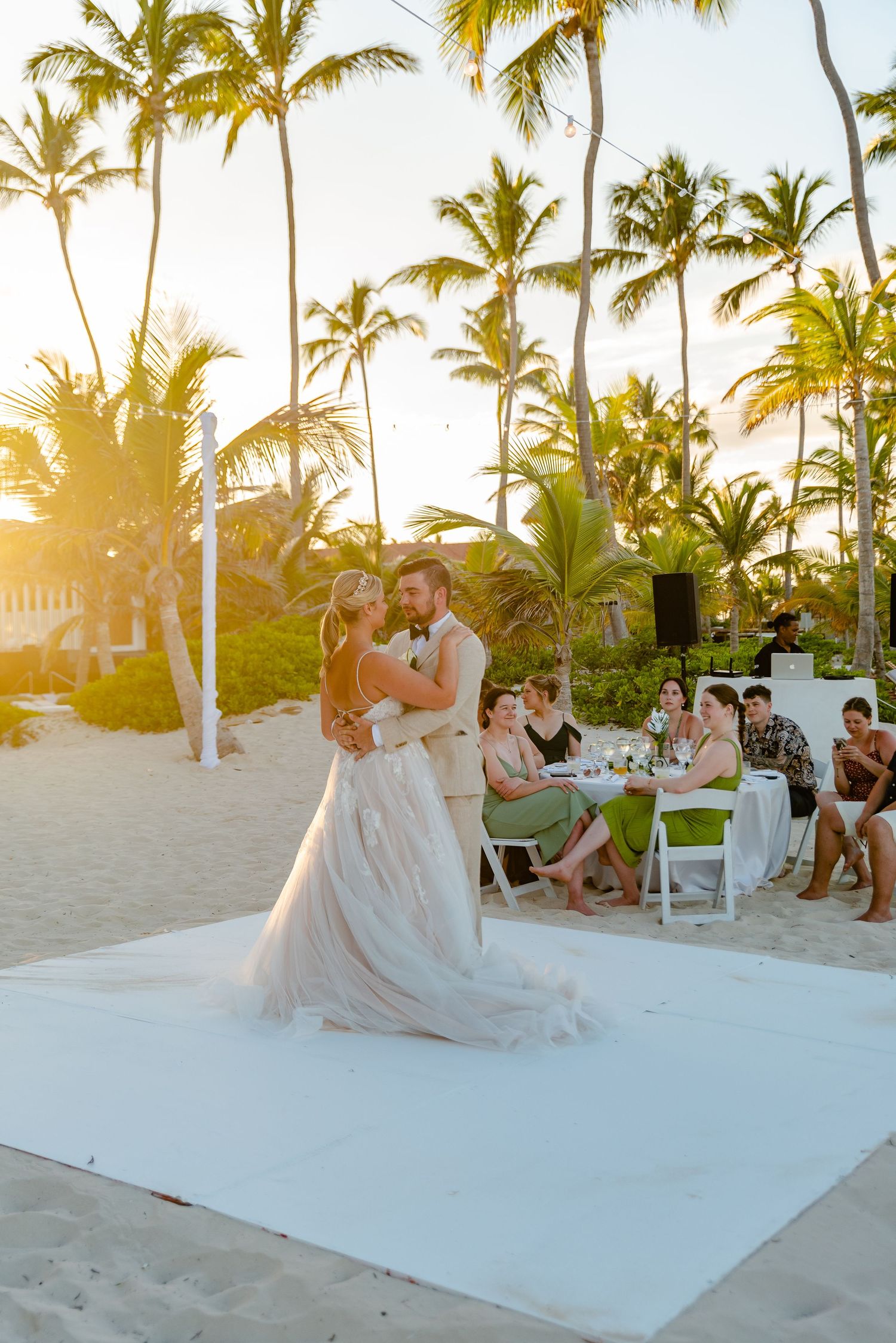 Newlyweds share first dance on white dance floor at golden sunset beach wedding reception.