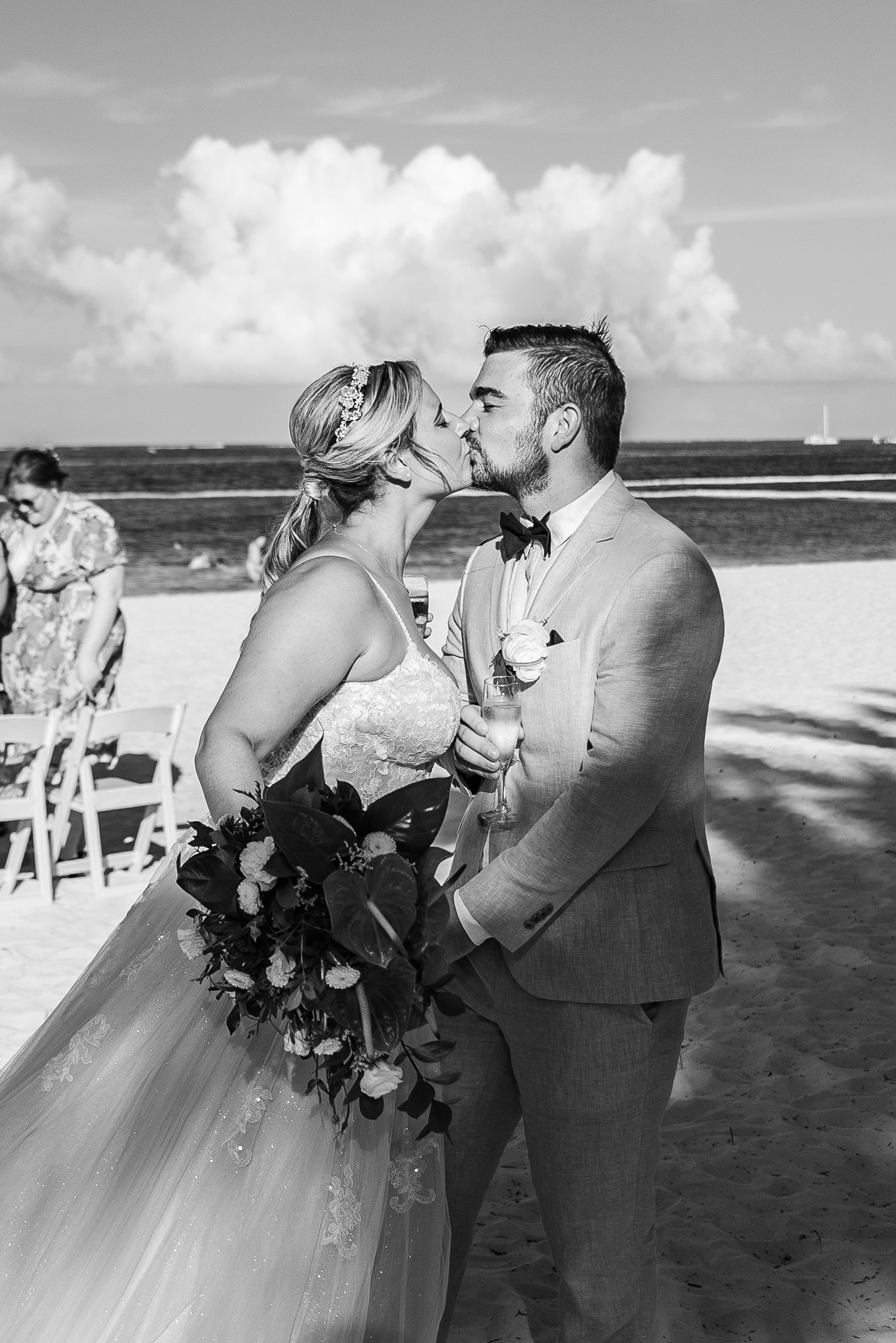 Bride and groom share first kiss on sandy beach in black and white wedding photo.