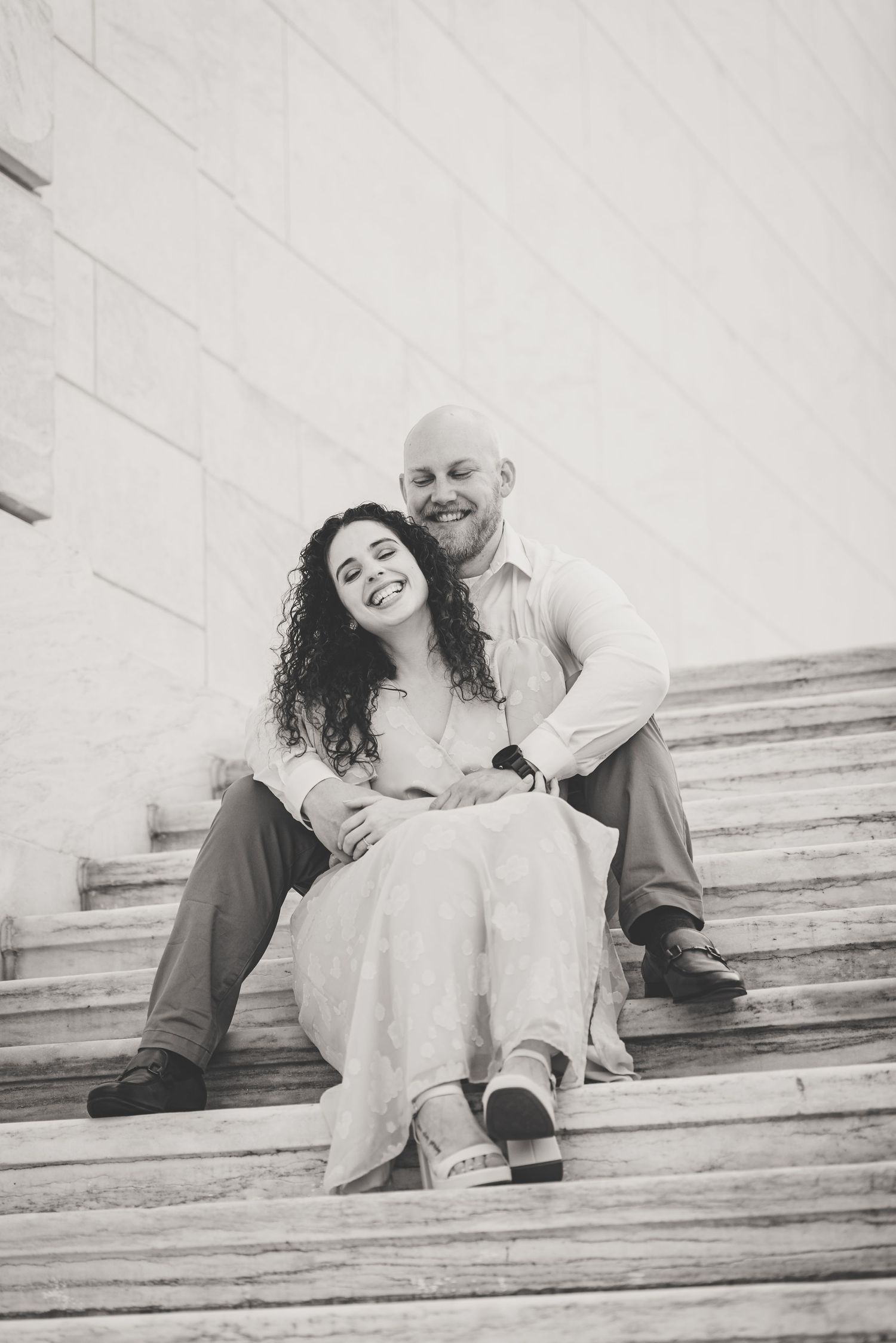 Happy couple sitting on stone steps embracing in black and white photo.