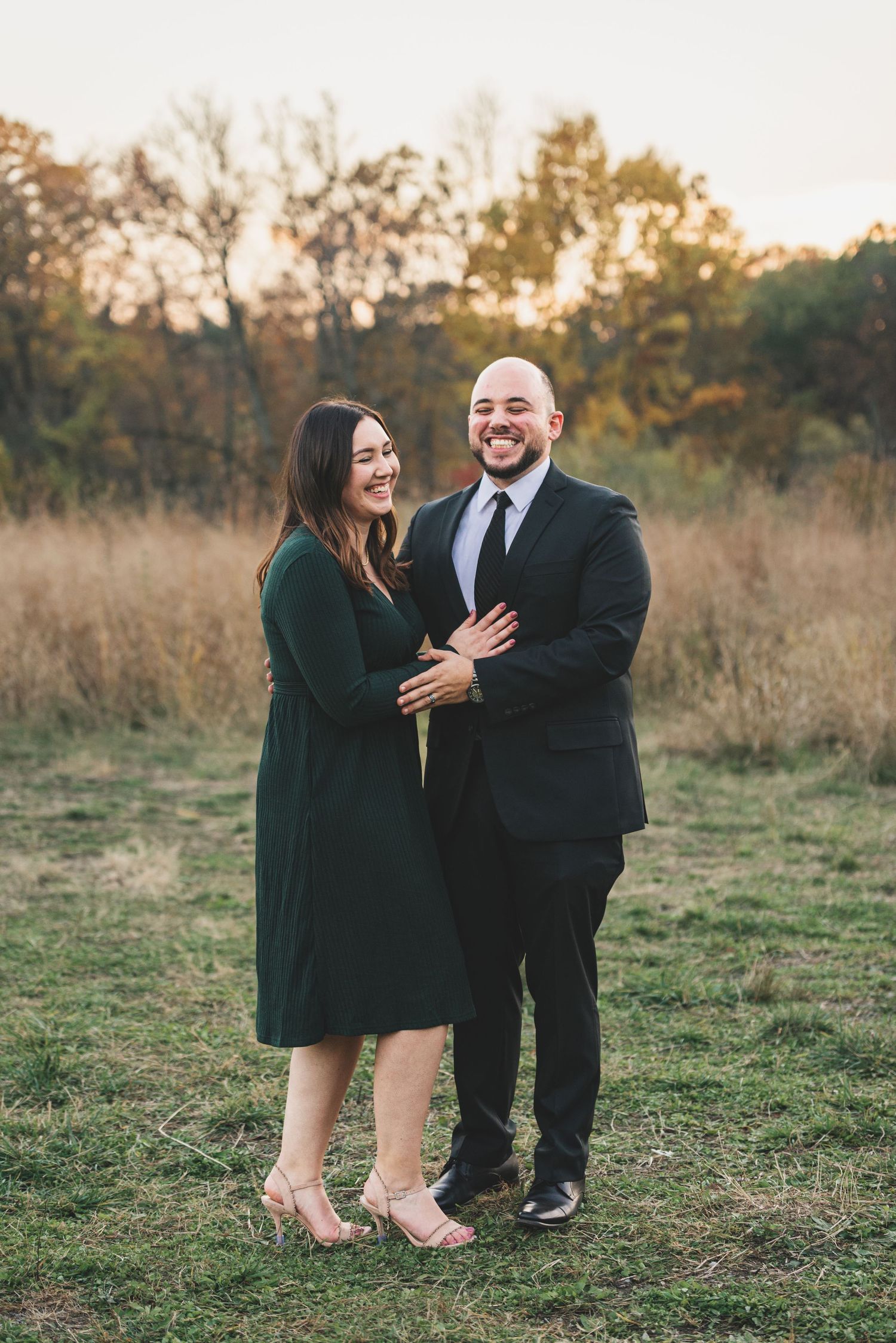 Happy couple laughing together in golden hour light during fall outdoor engagement photo session.