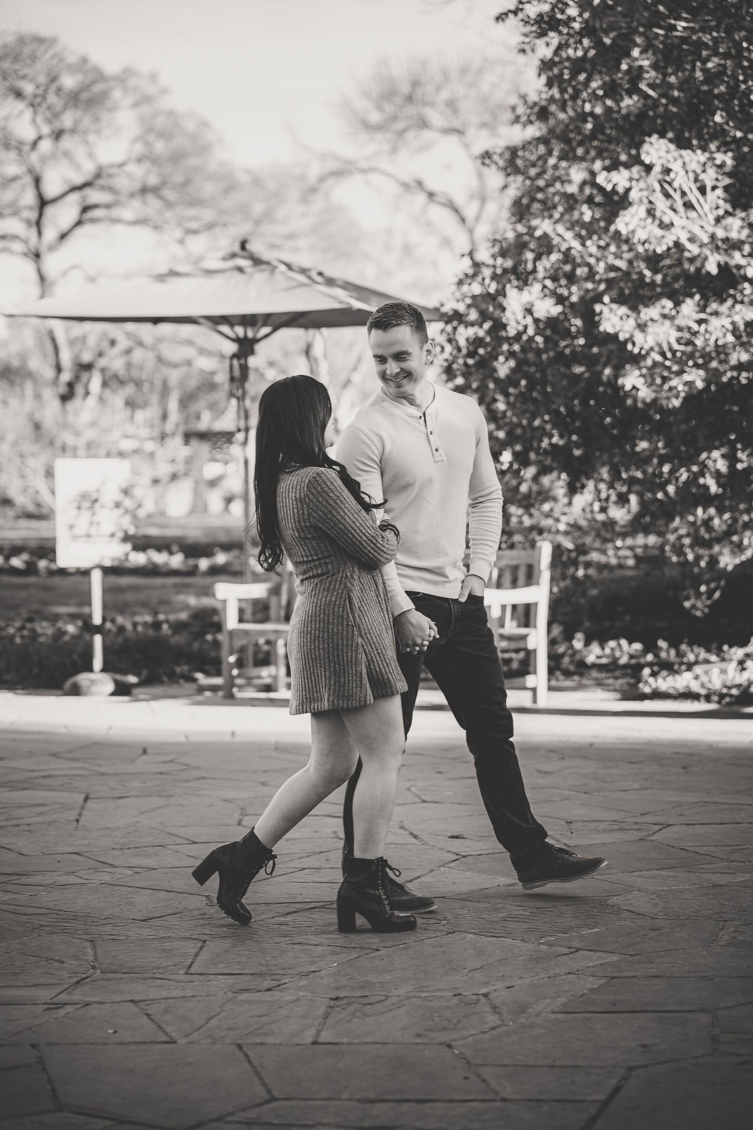 Black and white photo of a couple holding hands and smiling at each other on a stone patio in a garden.