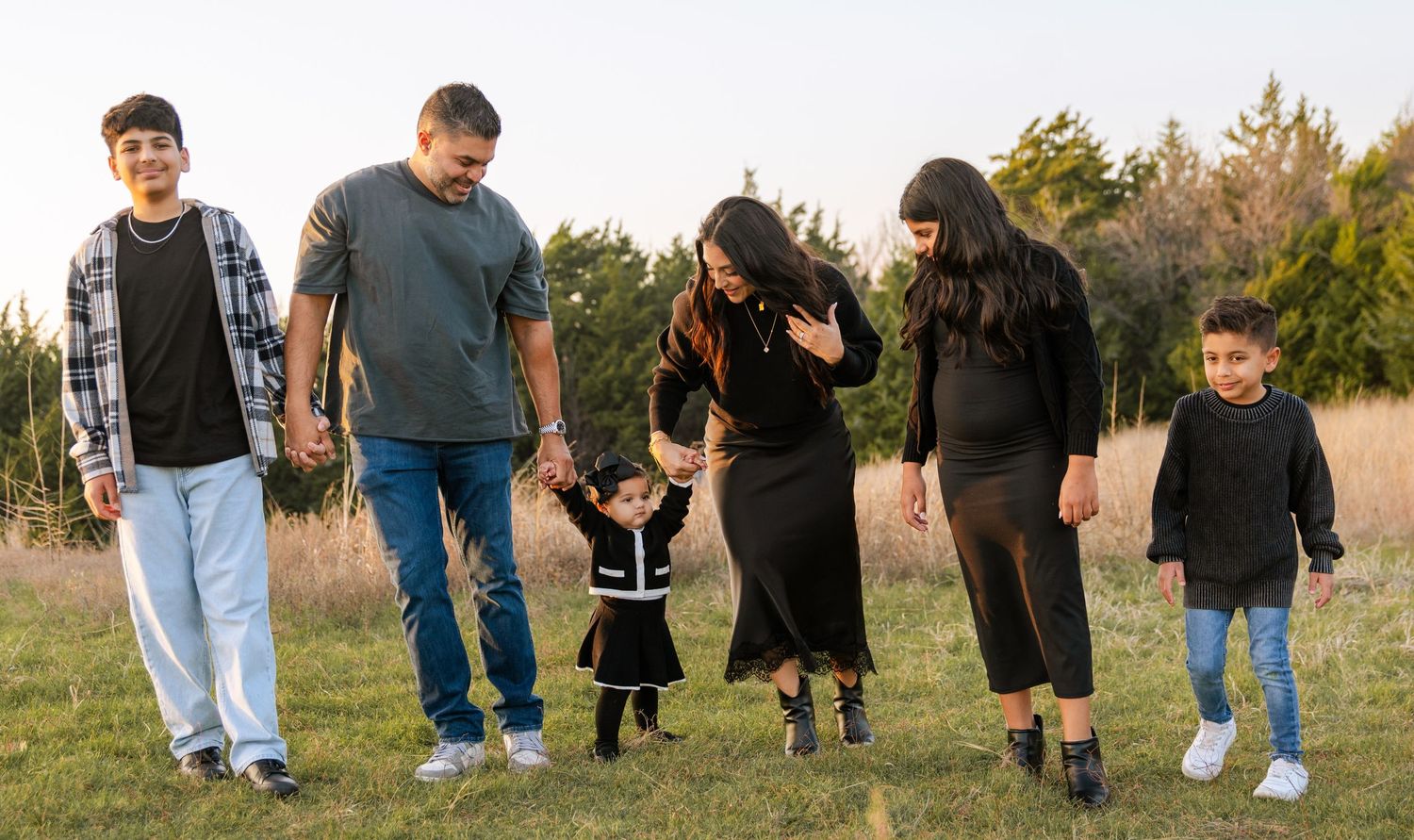 A happy family walks together hand-in-hand through a grassy field at golden hour.