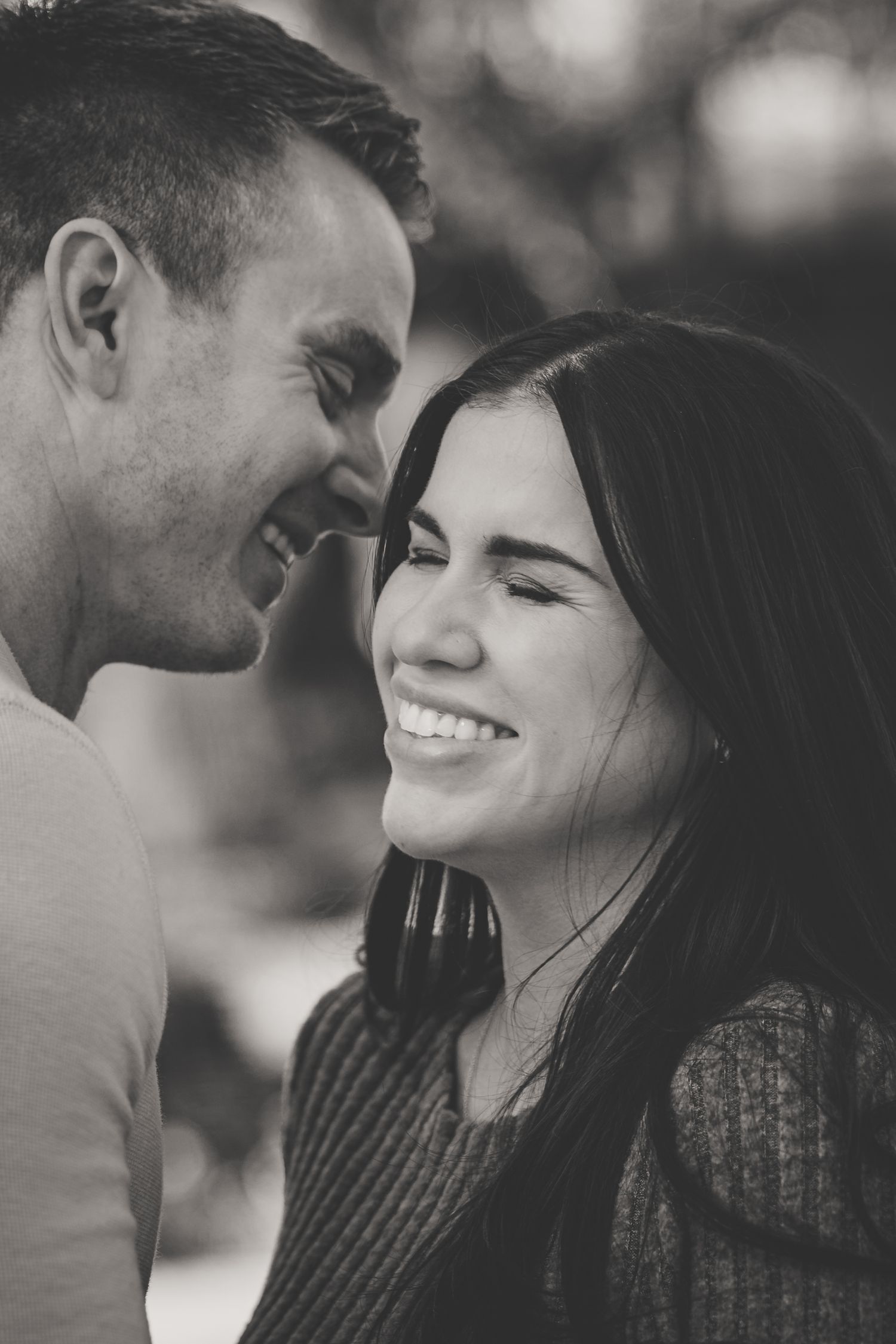 Black and white portrait of a laughing couple with foreheads close together sharing a joyful moment.