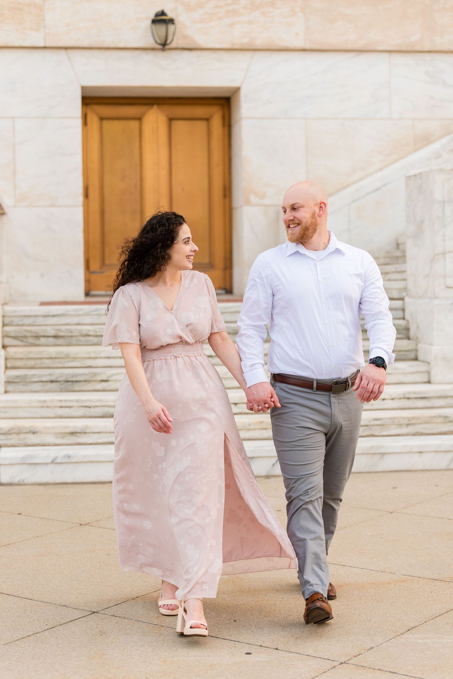 Couple holding hands and walking together in front of a grand stone building entrance.