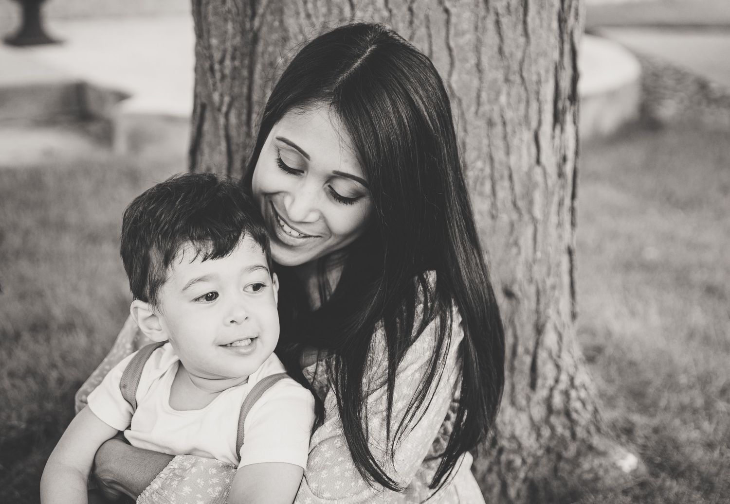 Smiling mother holding young child near tree in black and white portrait.