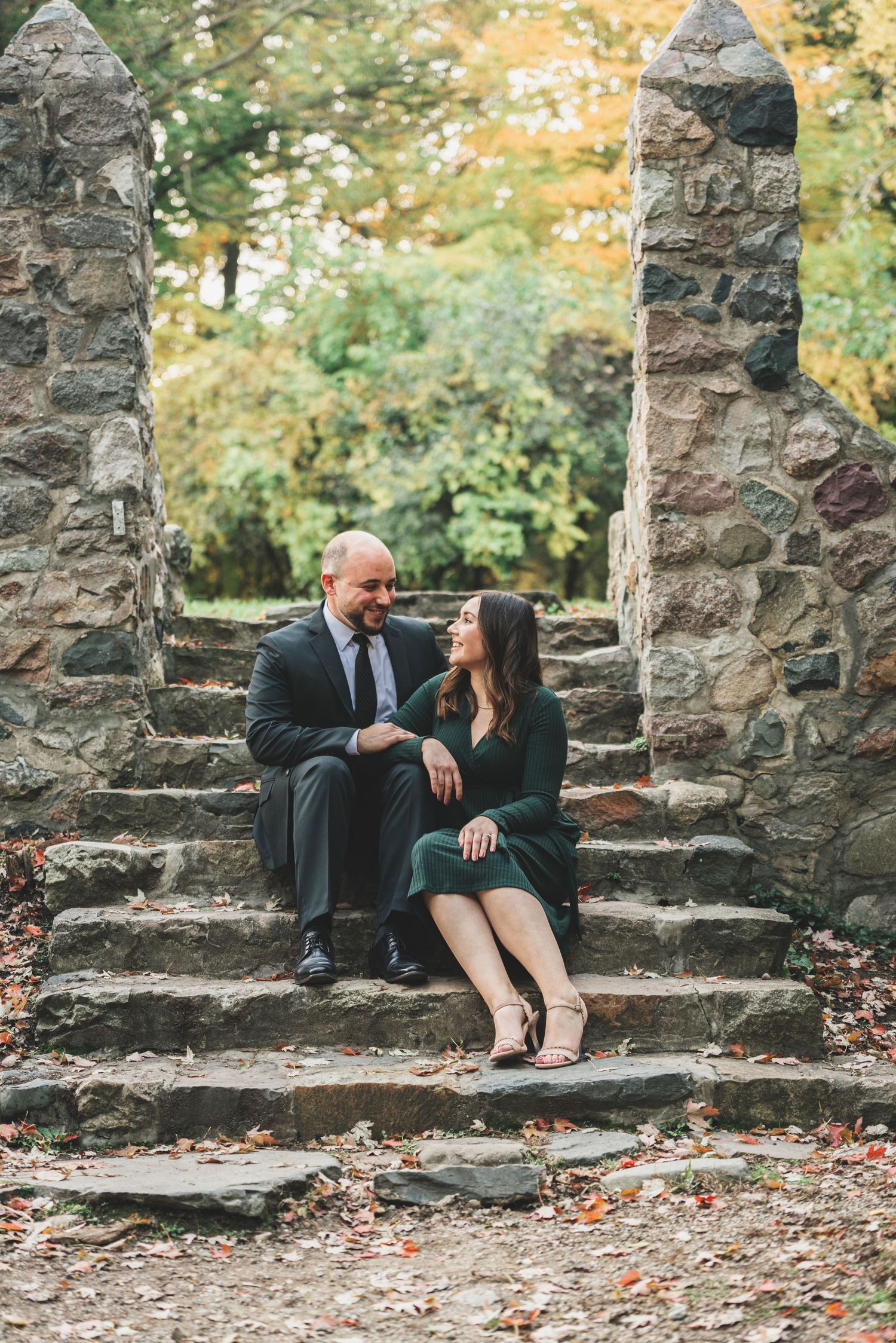 Couple sitting on rustic stone steps surrounded by autumn foliage during engagement photo session.